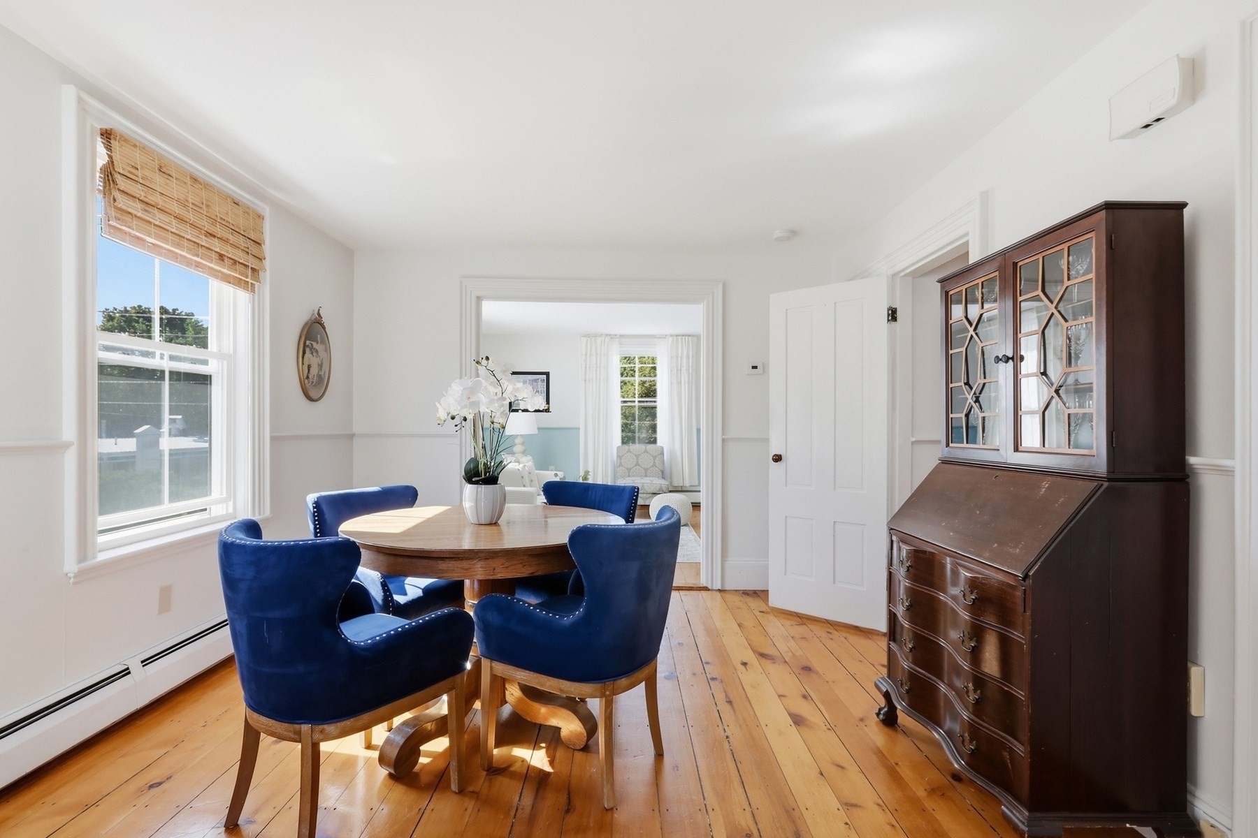 Dining room with a round table, blue chairs, wide-plank wood floors, and a dark secretary cabinet.