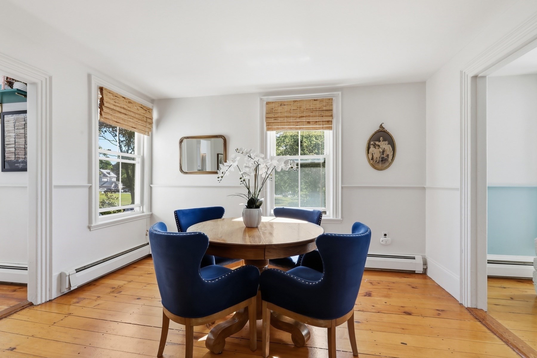 Dining room with a round wood table, navy chairs, orchid centerpiece, and sunny windows.