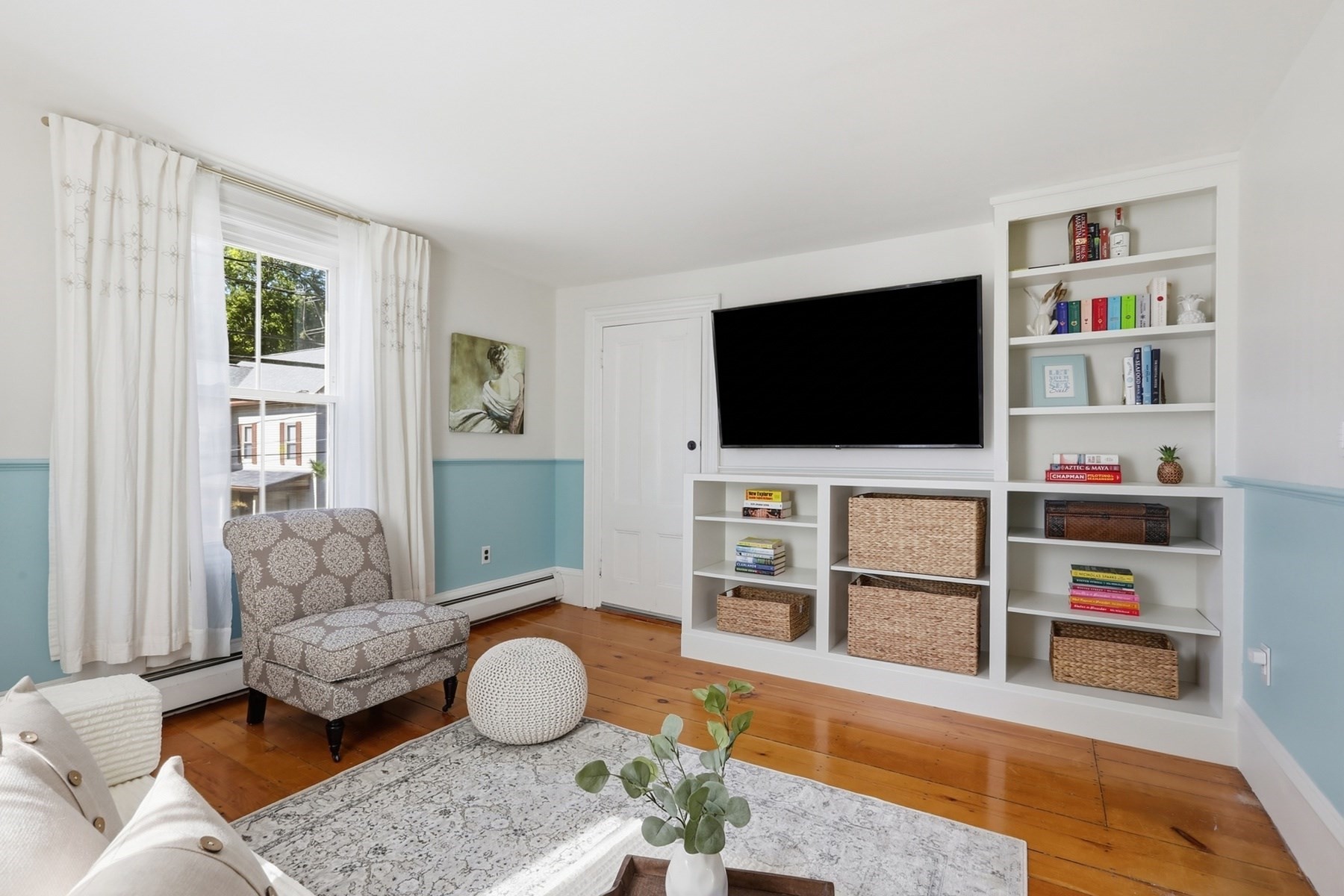 Living room with built-in white shelving, a wall-mounted TV, blue wainscoting, and warm wood floors.