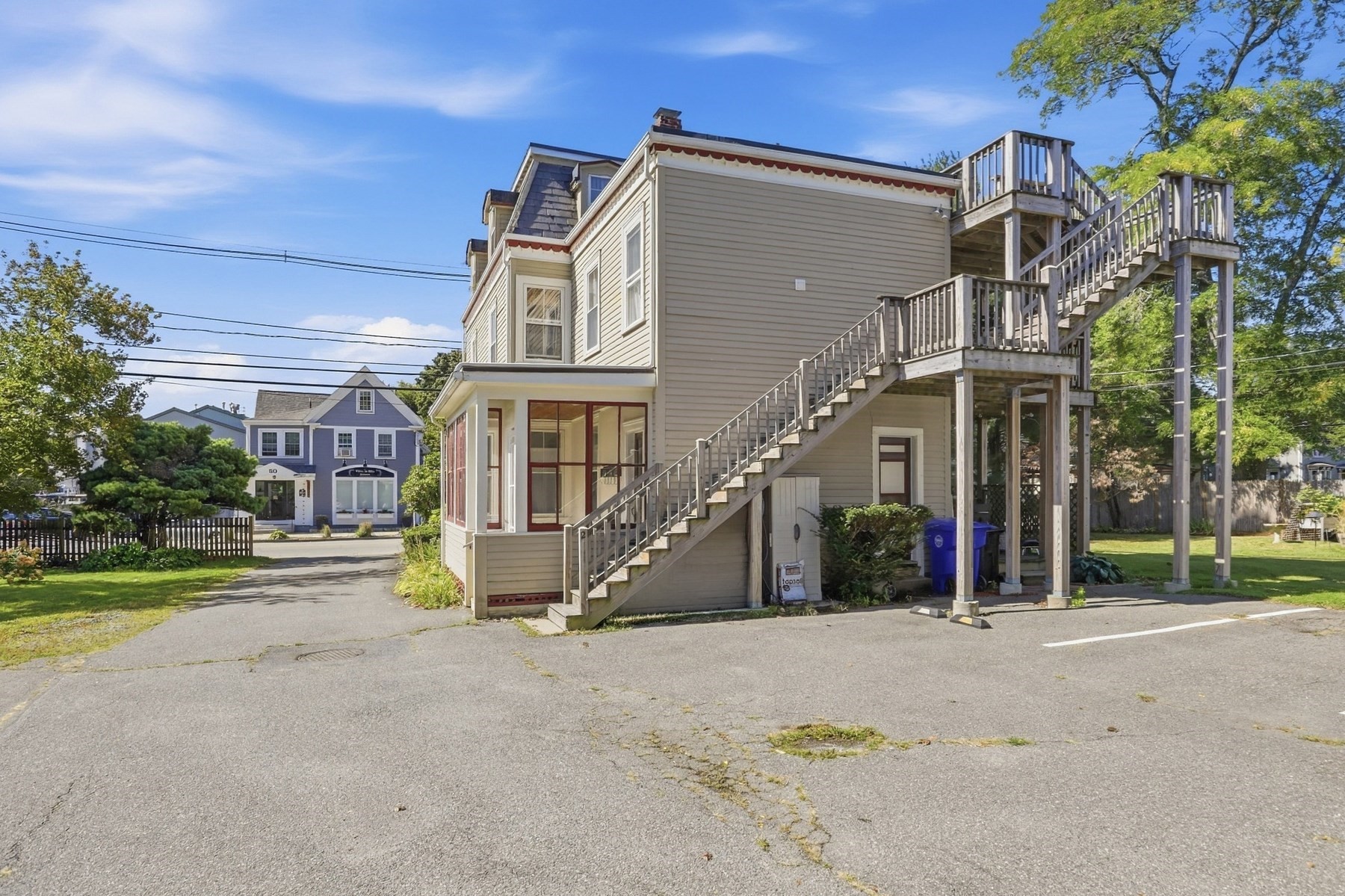 Beige-sided home with a red-trimmed enclosed porch and large exterior staircase to elevated decks.