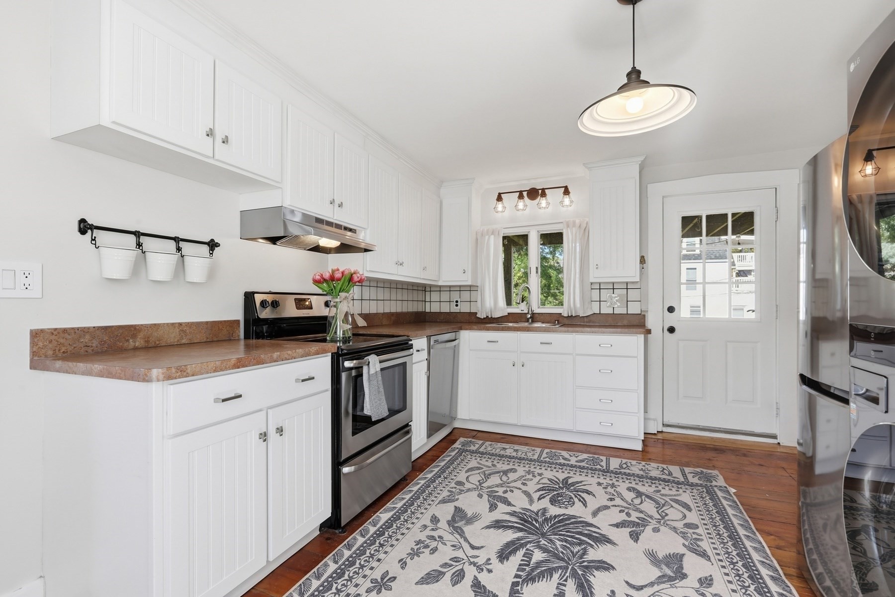 Bright white kitchen with brown countertops, stainless appliances, and a patterned rug on hardwood floors.