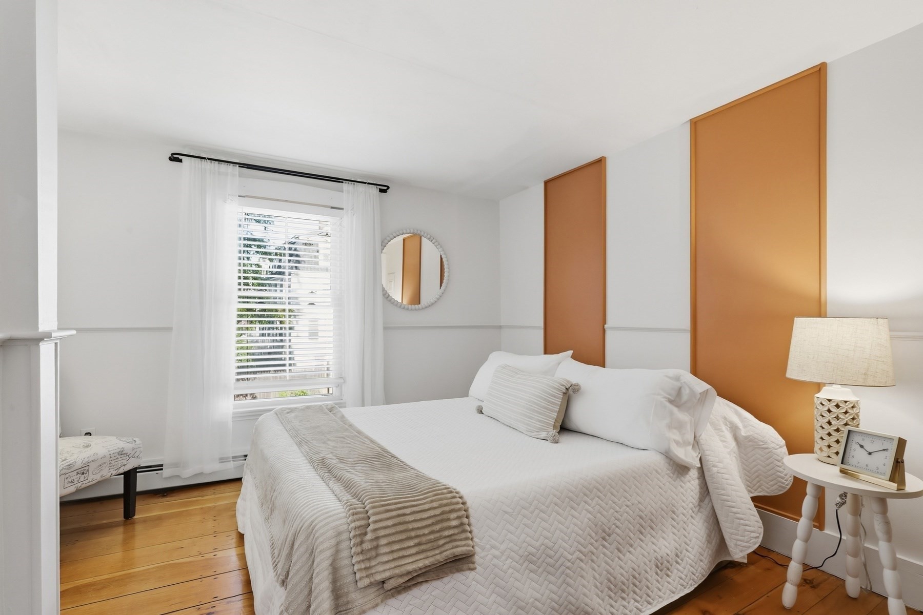 Bright bedroom with a white quilted bed, warm wood floors, and orange wall panels.
