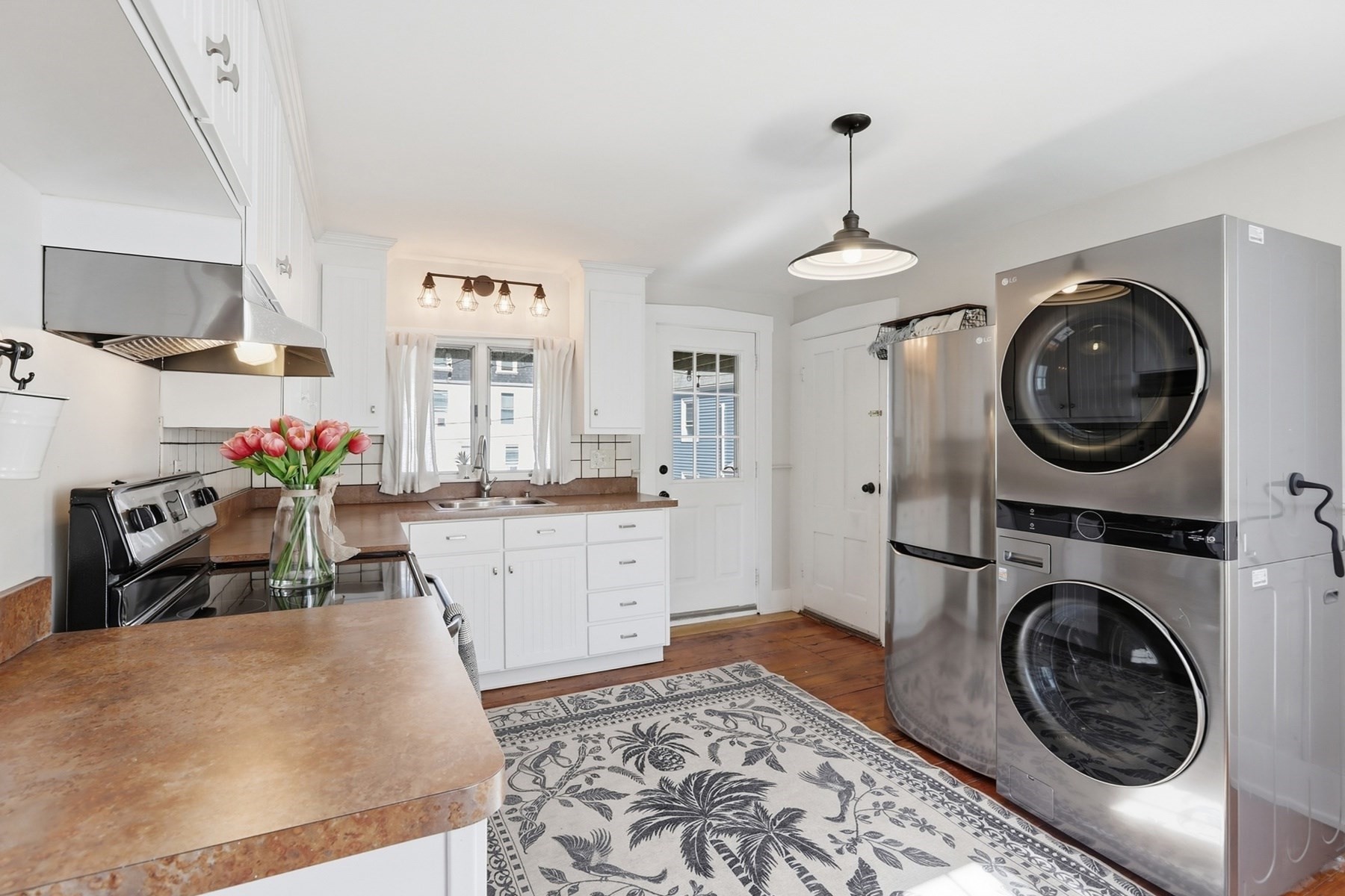 Kitchen with white cabinetry, a sink beneath curtained windows, and stacked stainless washer and dryer.