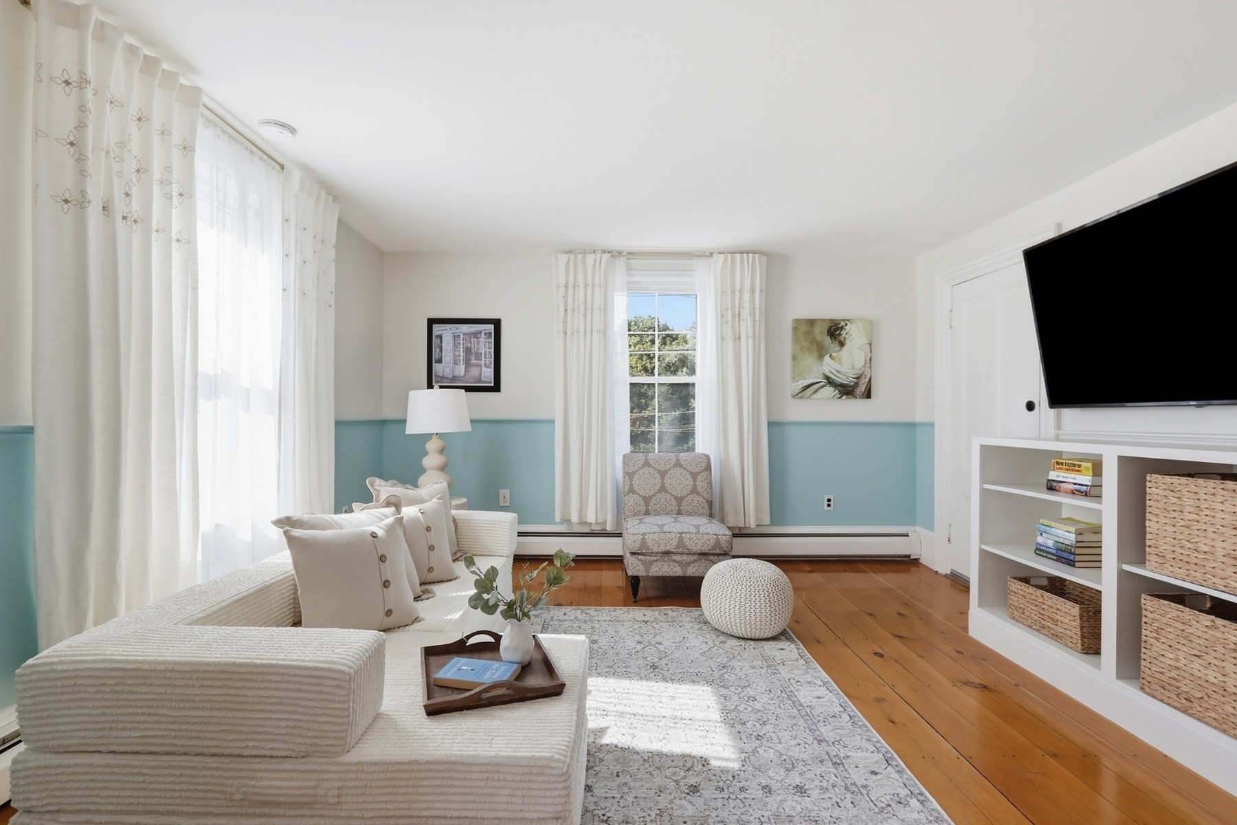 Living room with a white sectional, turquoise wainscoting, hardwood floors, and tall curtained windows.