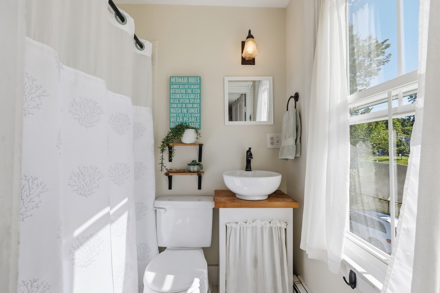 Bright bathroom with a coral-pattern shower curtain, wood-countertop vessel sink, and large curtained window.