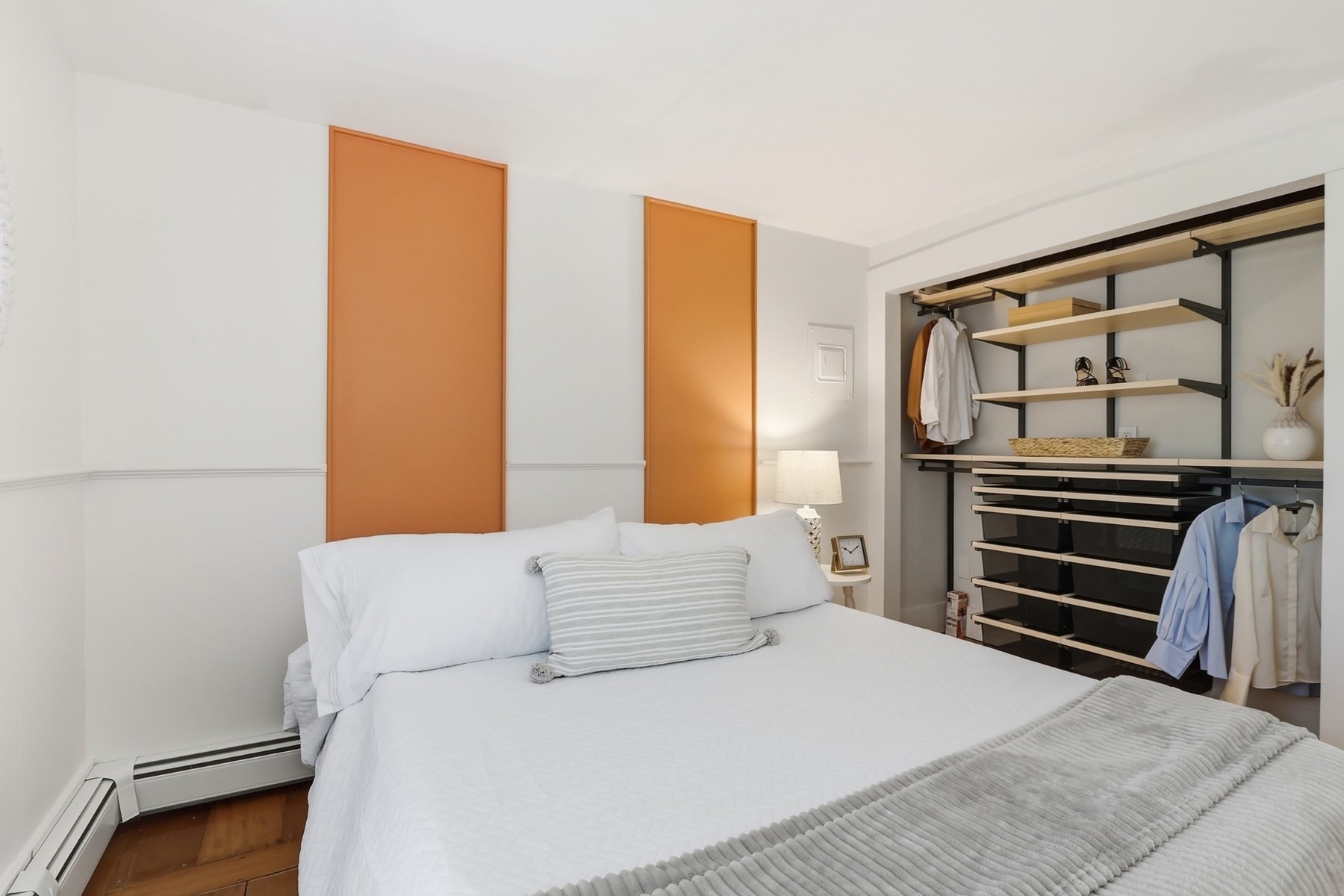 Bedroom with a white bed, orange wall panels, and an open wardrobe with shelving.