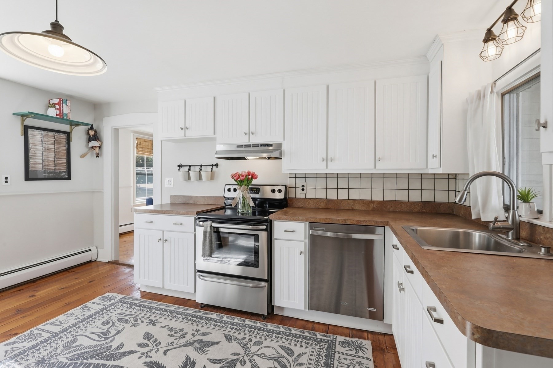 Bright kitchen with white cabinets, stainless steel appliances, brown counters, and a double-basin sink.