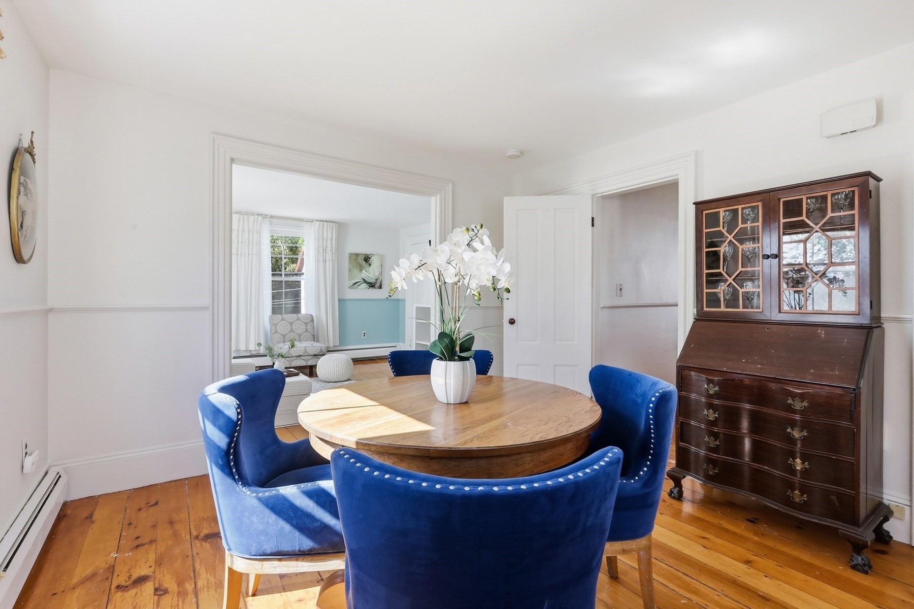 Dining room with a round wooden table, blue chairs, hardwood floors, and a dark secretary cabinet.