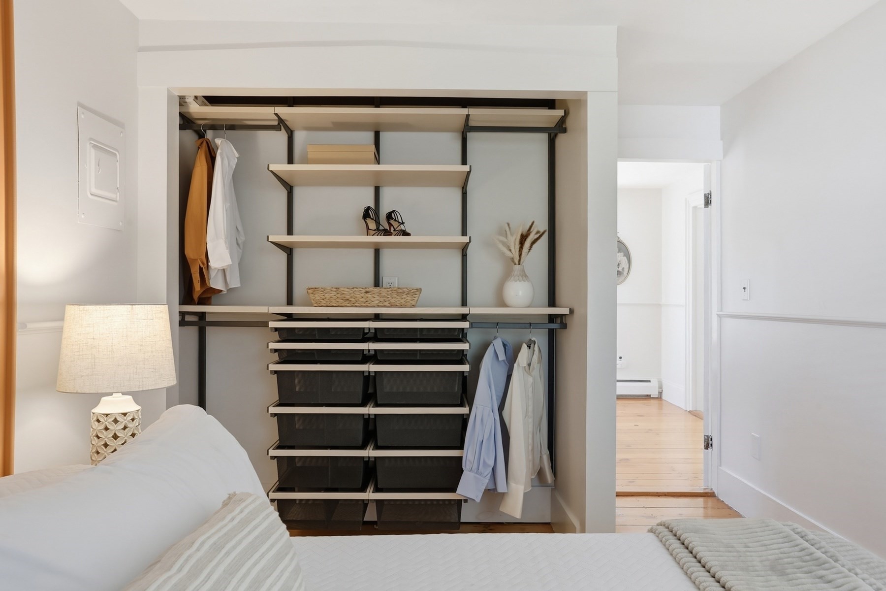 Bedroom with a bed and an open closet fitted with shelves, hanging clothes, and storage baskets.