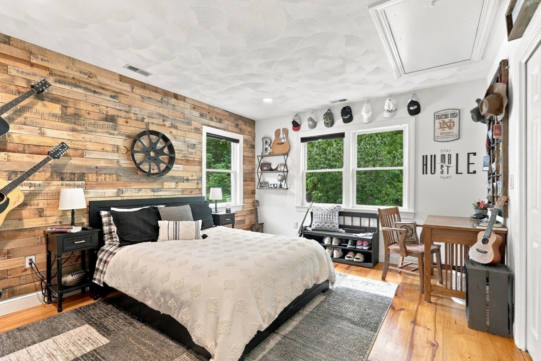 Bedroom with a reclaimed wood accent wall, black bed, guitars, and windows overlooking greenery.