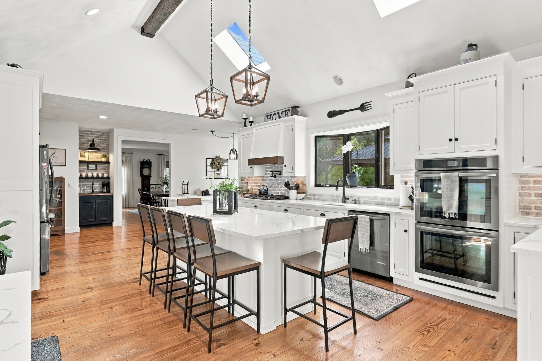 Bright kitchen with a large island, white cabinets, stainless double ovens, and vaulted ceiling with wood beams.