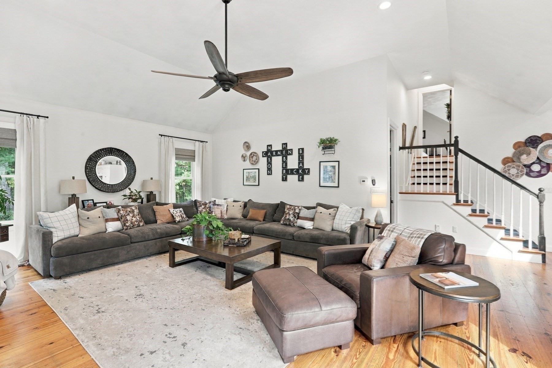 Vaulted living room with a large sectional, leather chairs, and a staircase with dark railings.
