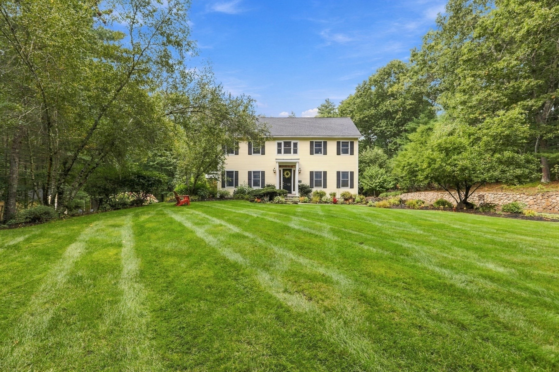 Two-story yellow house with dark shutters behind a broad striped lawn and mature trees.