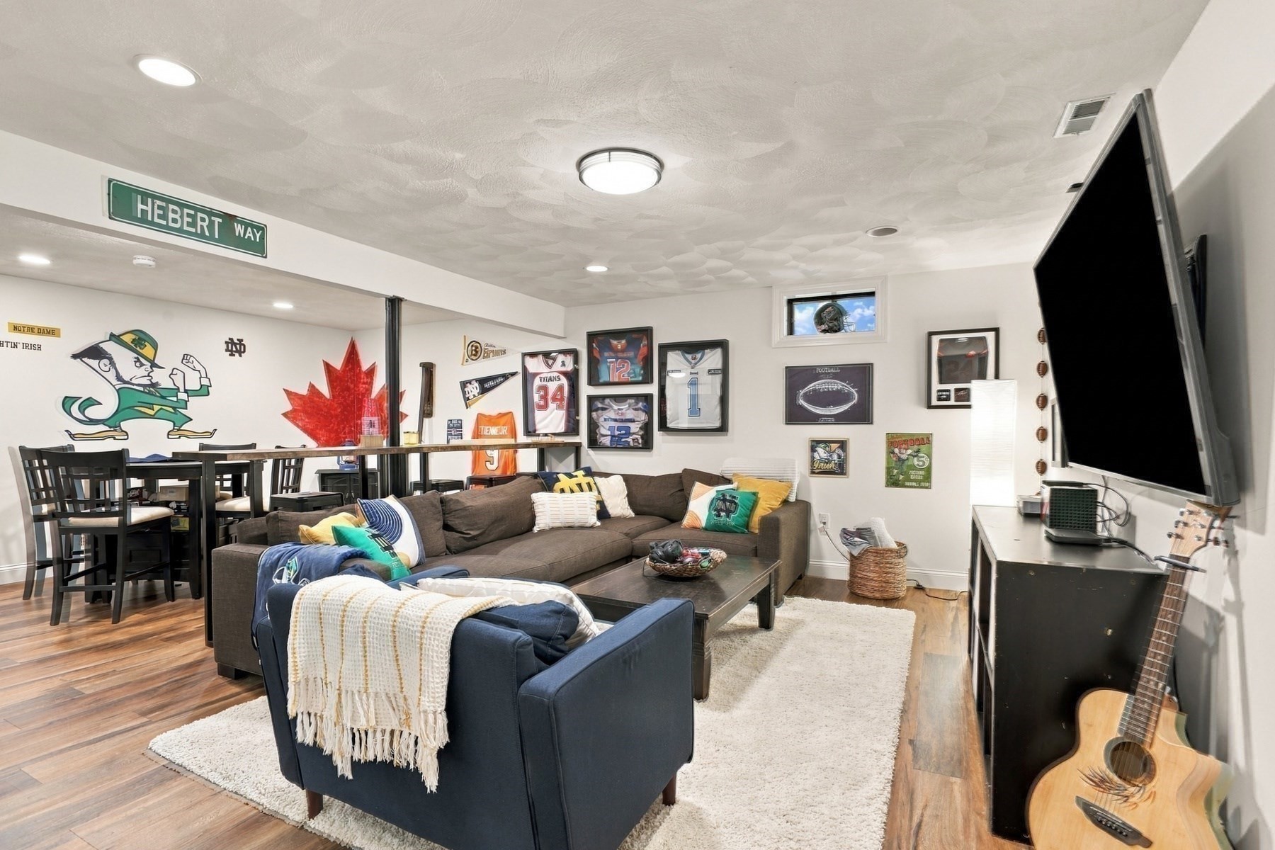 Furnished basement family room with a sectional, large television, sports memorabilia, Notre Dame mural, and guitar.