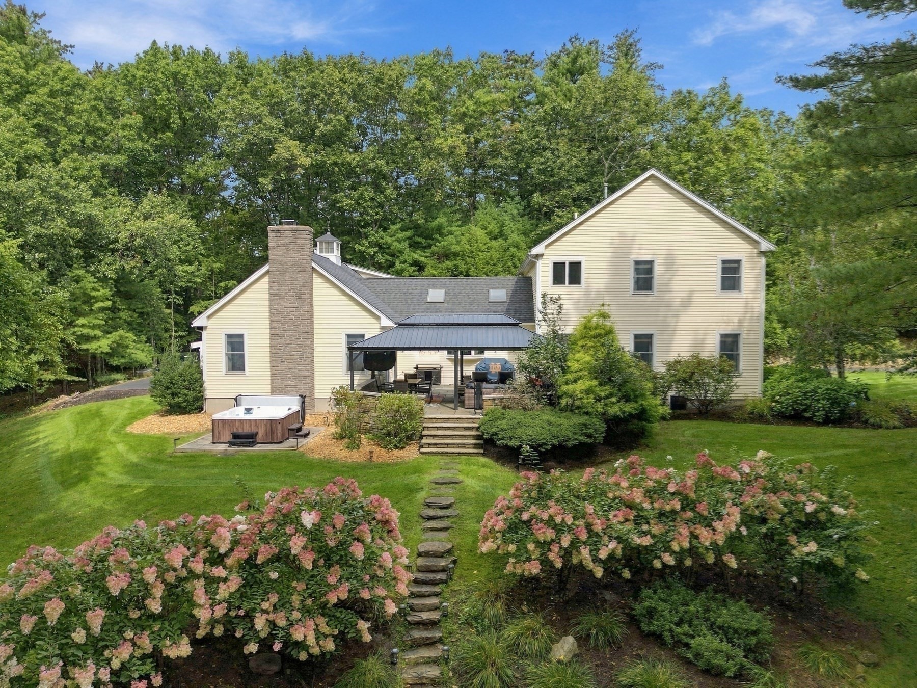 Yellow home’s landscaped backyard with a covered patio, hot tub, and stepping-stone path.