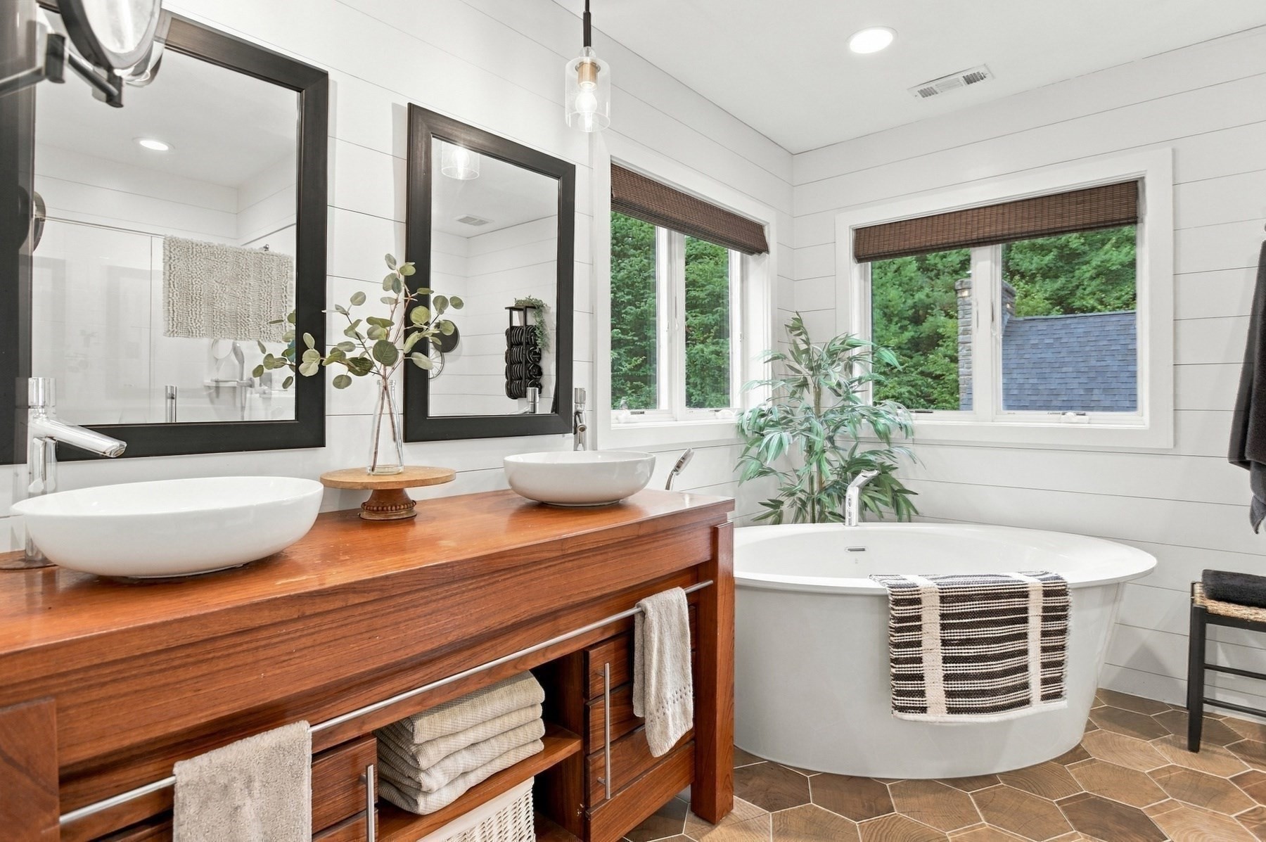 Bathroom with a freestanding soaking tub, double vessel sinks, and windows overlooking trees.