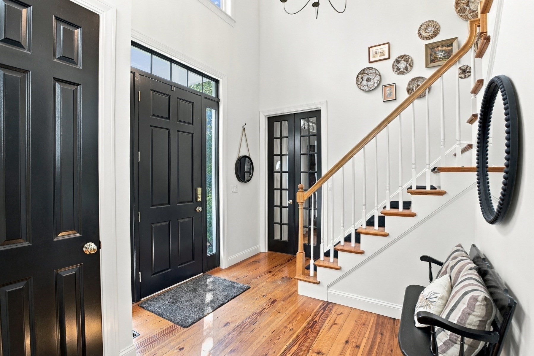 Bright entryway with a black front door, hardwood floors, and a staircase with a wood handrail.