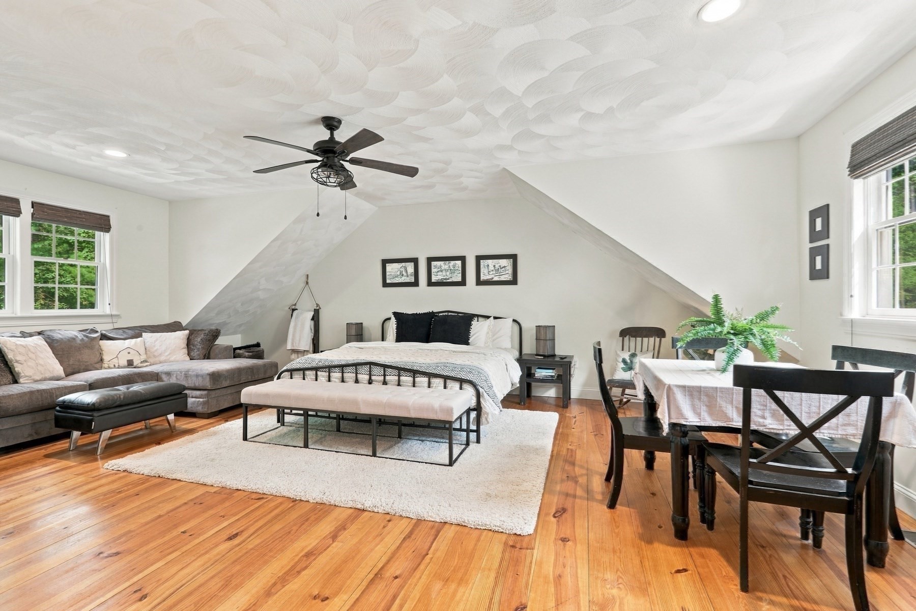 Bedroom with a patterned sloped ceiling, hardwood floors, bed, sofa, and dining table.
