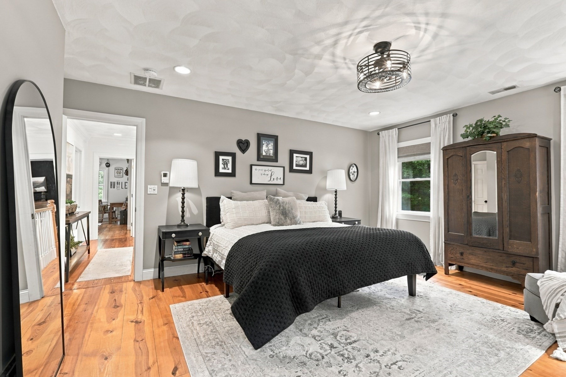 Furnished bedroom with a black-covered bed, patterned rug, warm wood floors, and a dark wood wardrobe.