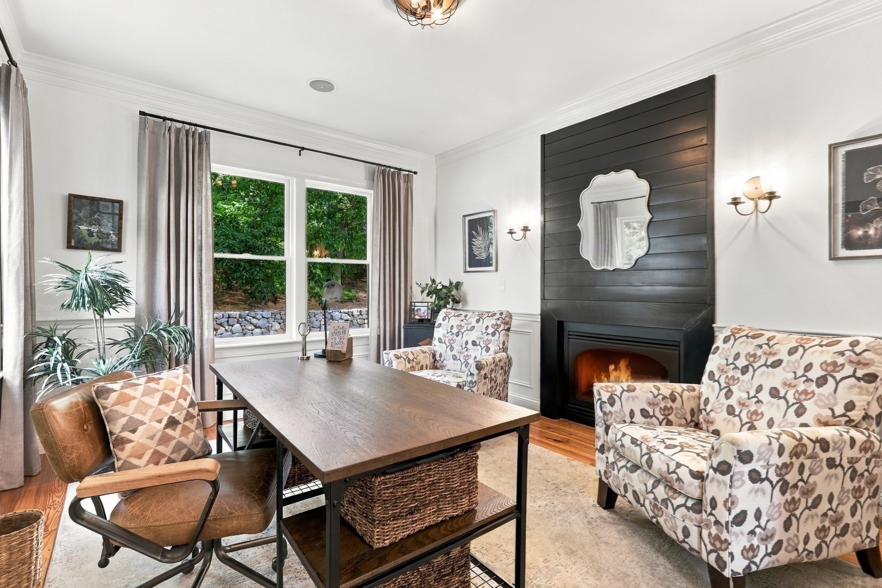 Sitting room with a dark paneled fireplace, patterned seating, and windows overlooking greenery.