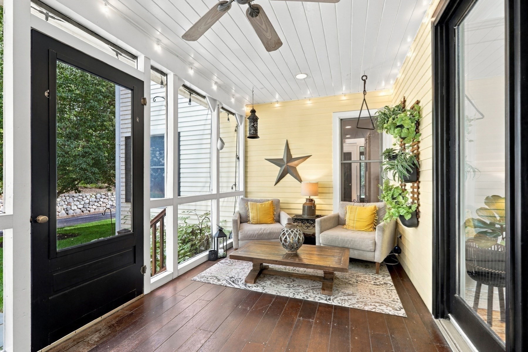 Enclosed porch with yellow walls, large windows, two cushioned chairs, and a wooden coffee table.