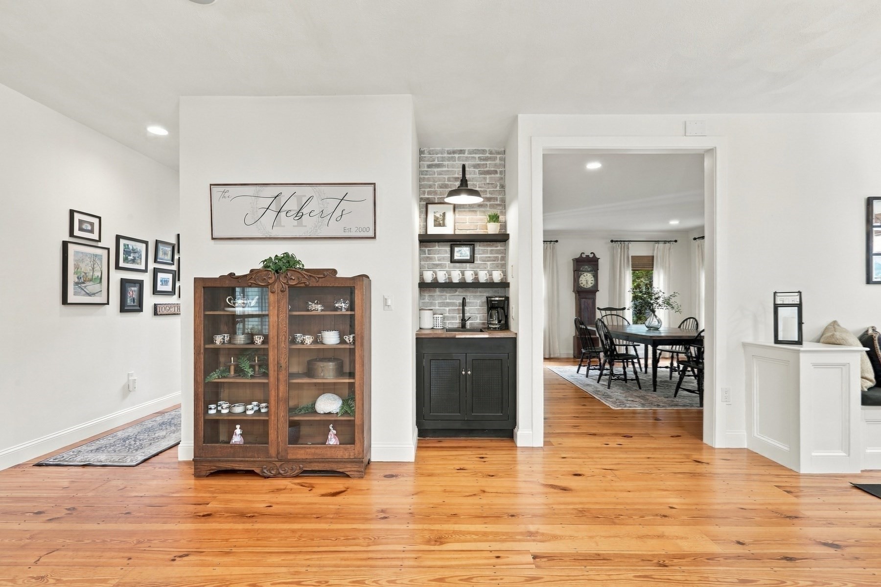 Living area with wide-plank wood floors, a brick-backed coffee bar, and adjoining dining room.