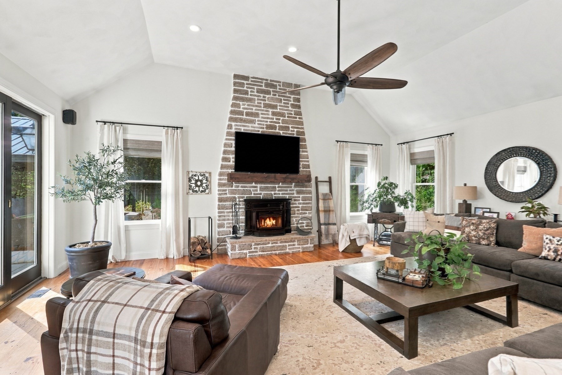 Living room with a vaulted ceiling and stone fireplace, furnished with dark leather seating.