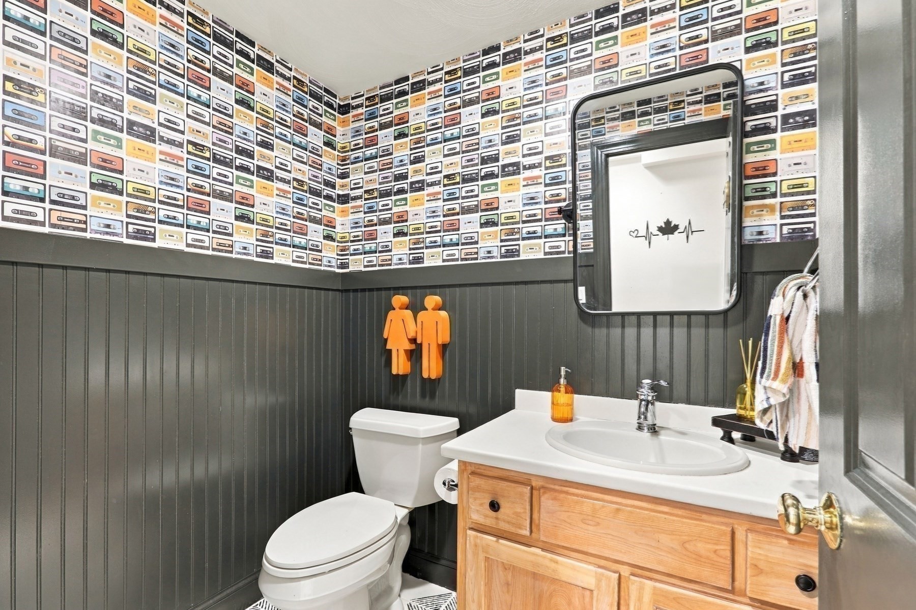 Bathroom with cassette-tape wallpaper, dark paneled walls, and a light wood vanity.