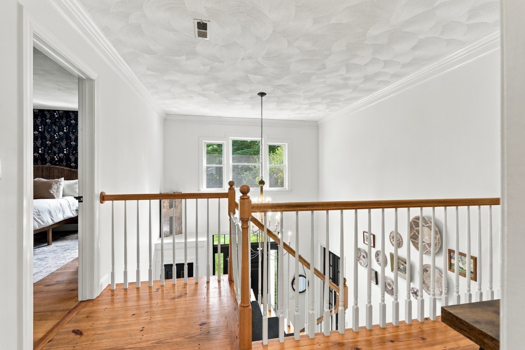 Upstairs landing with a wood-railed staircase, wide-plank floors, and a bedroom doorway.