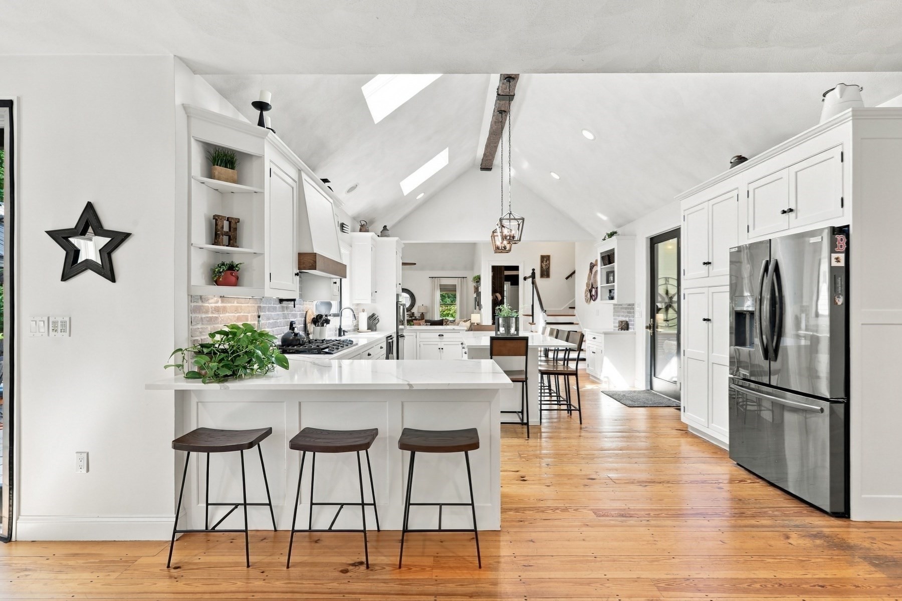 Bright kitchen with a vaulted skylit ceiling, white island, three stools, and stainless steel refrigerator.