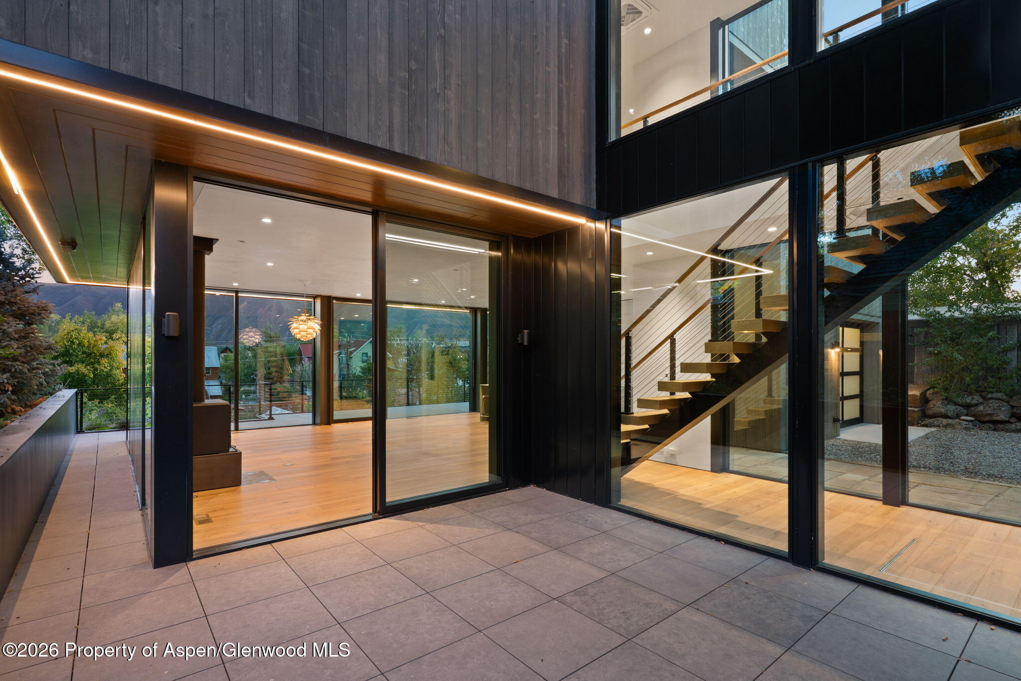 Modern home with floor-to-ceiling glass, dark siding, and an illuminated open staircase.