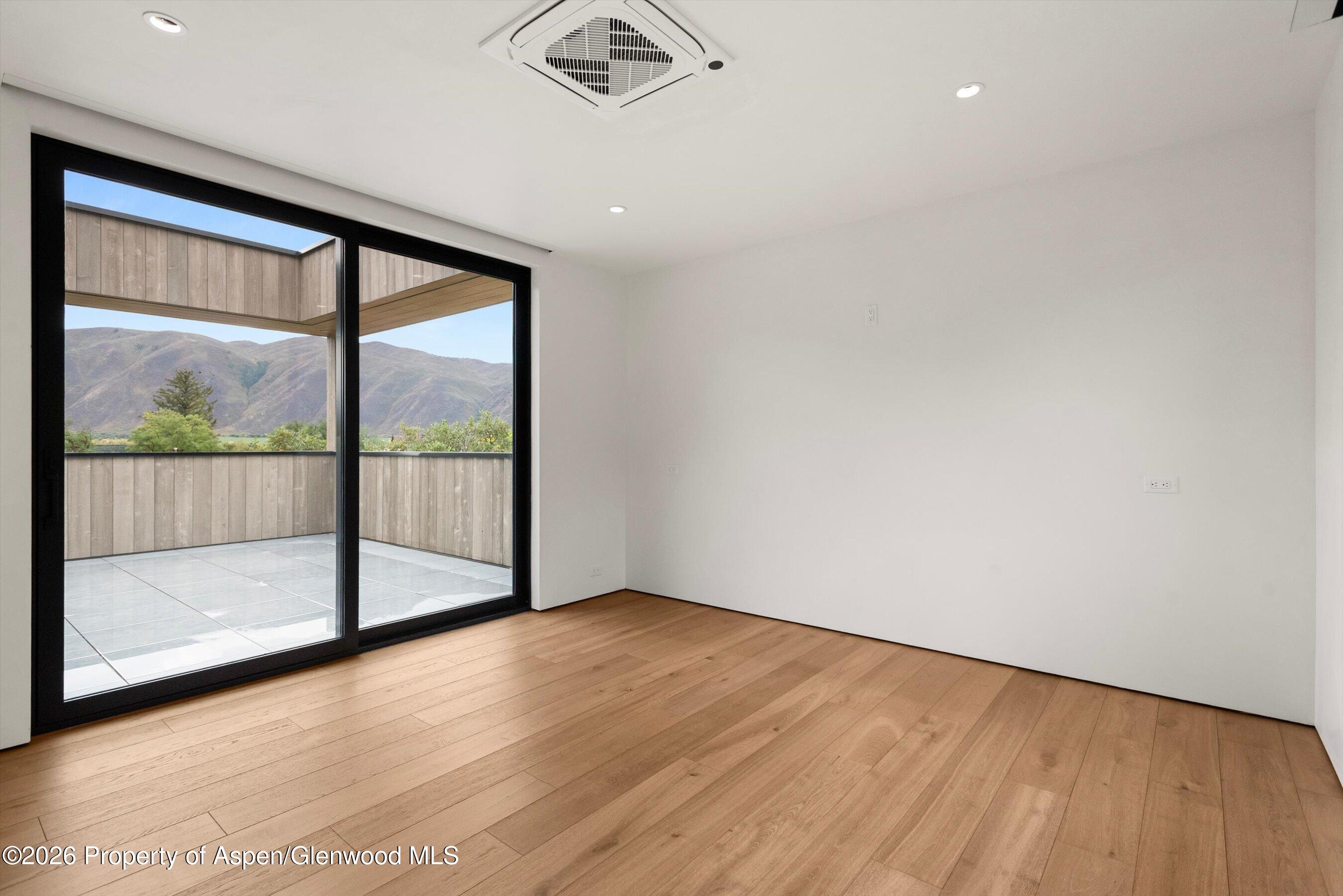 Empty modern room with wood floors and sliding doors opening onto a mountain-view terrace.