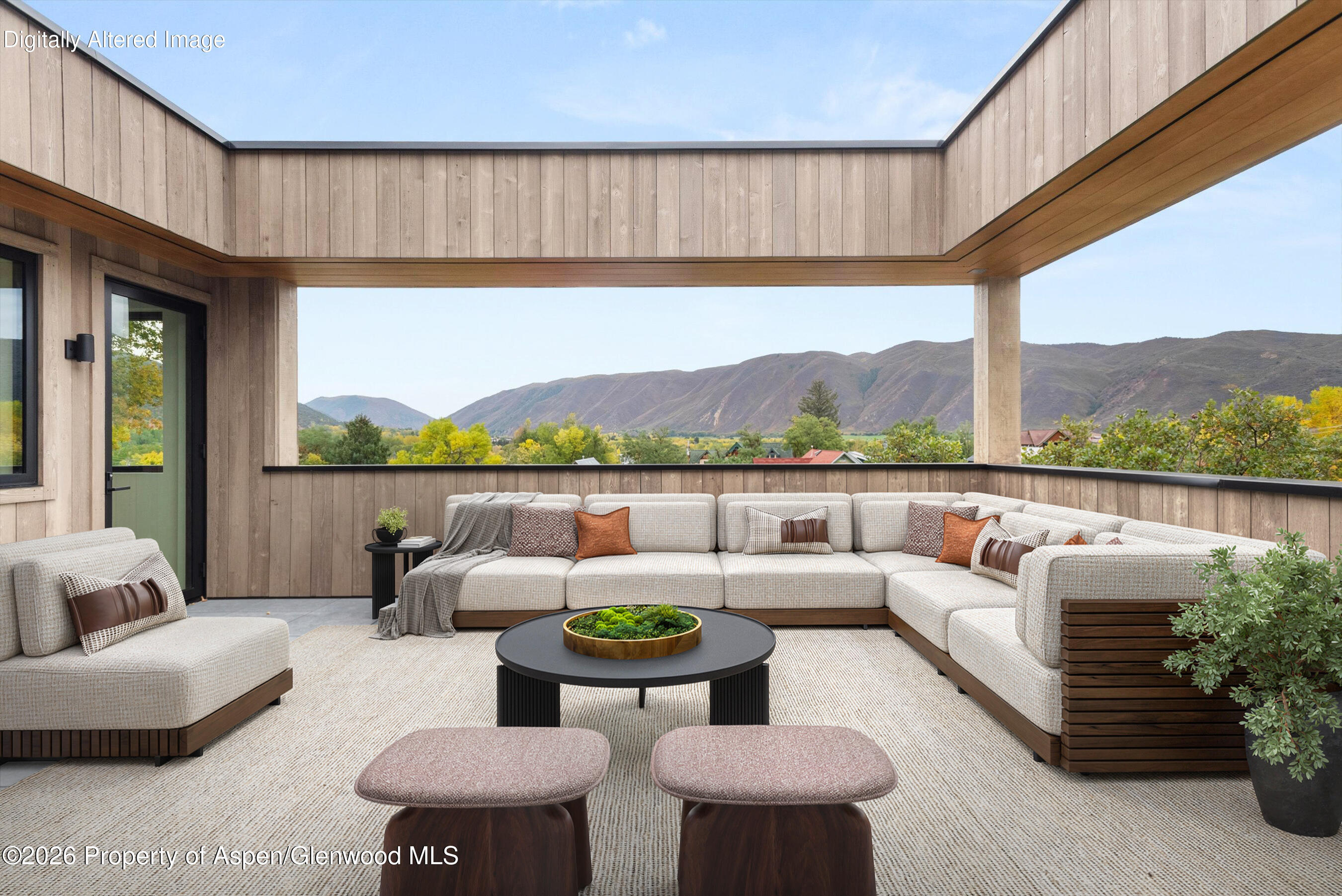 Covered patio with a cream sectional and mountain views beyond the open wood-paneled walls.