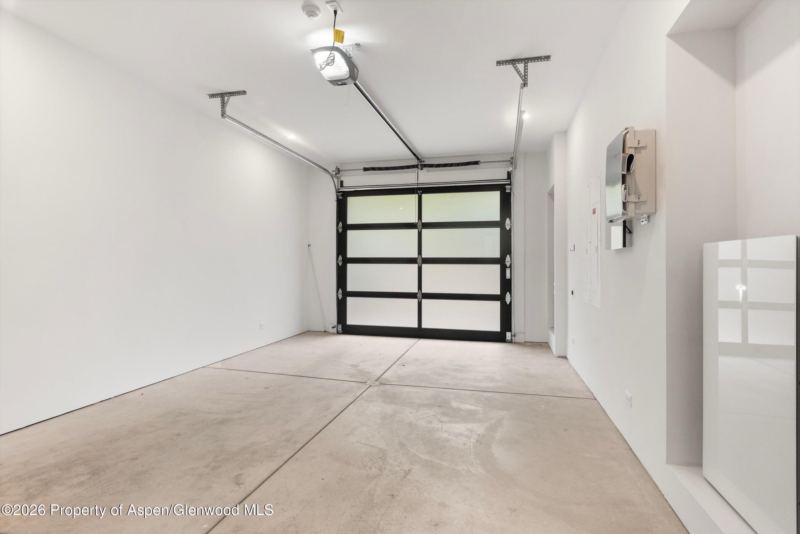 Empty garage with a black-framed sectional door, concrete floor, and wall-mounted EV charger.