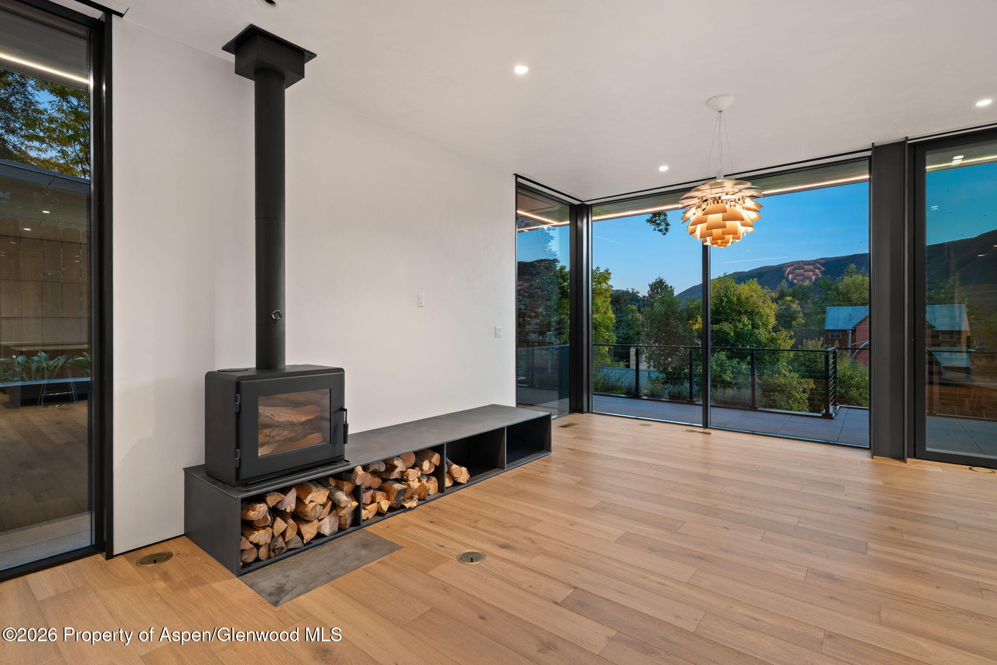 Modern living room with a black wood stove, corner windows, and mountain views from the balcony.