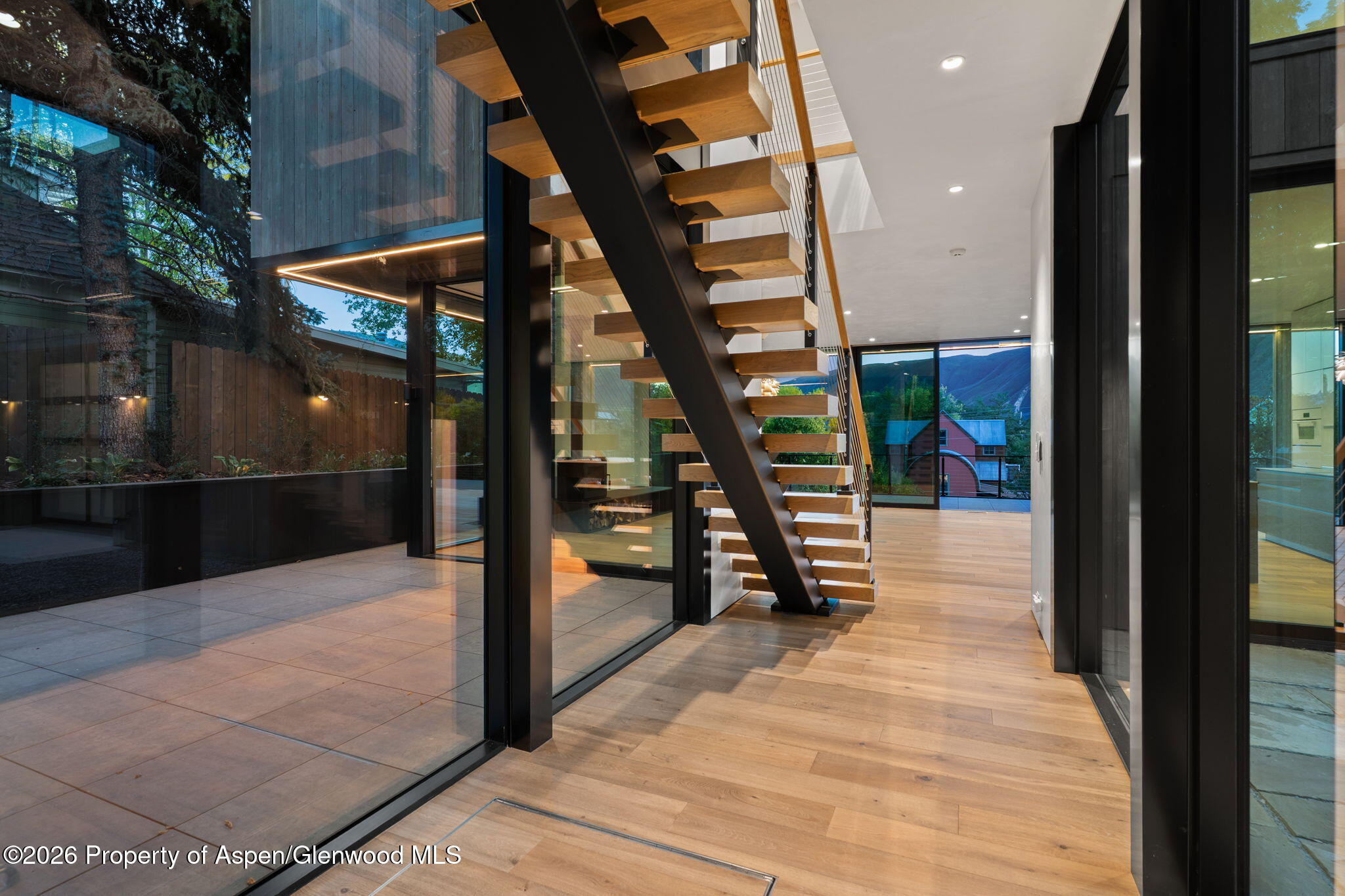 Modern entry hall with an open-riser wood staircase, glass walls, and mountain views.