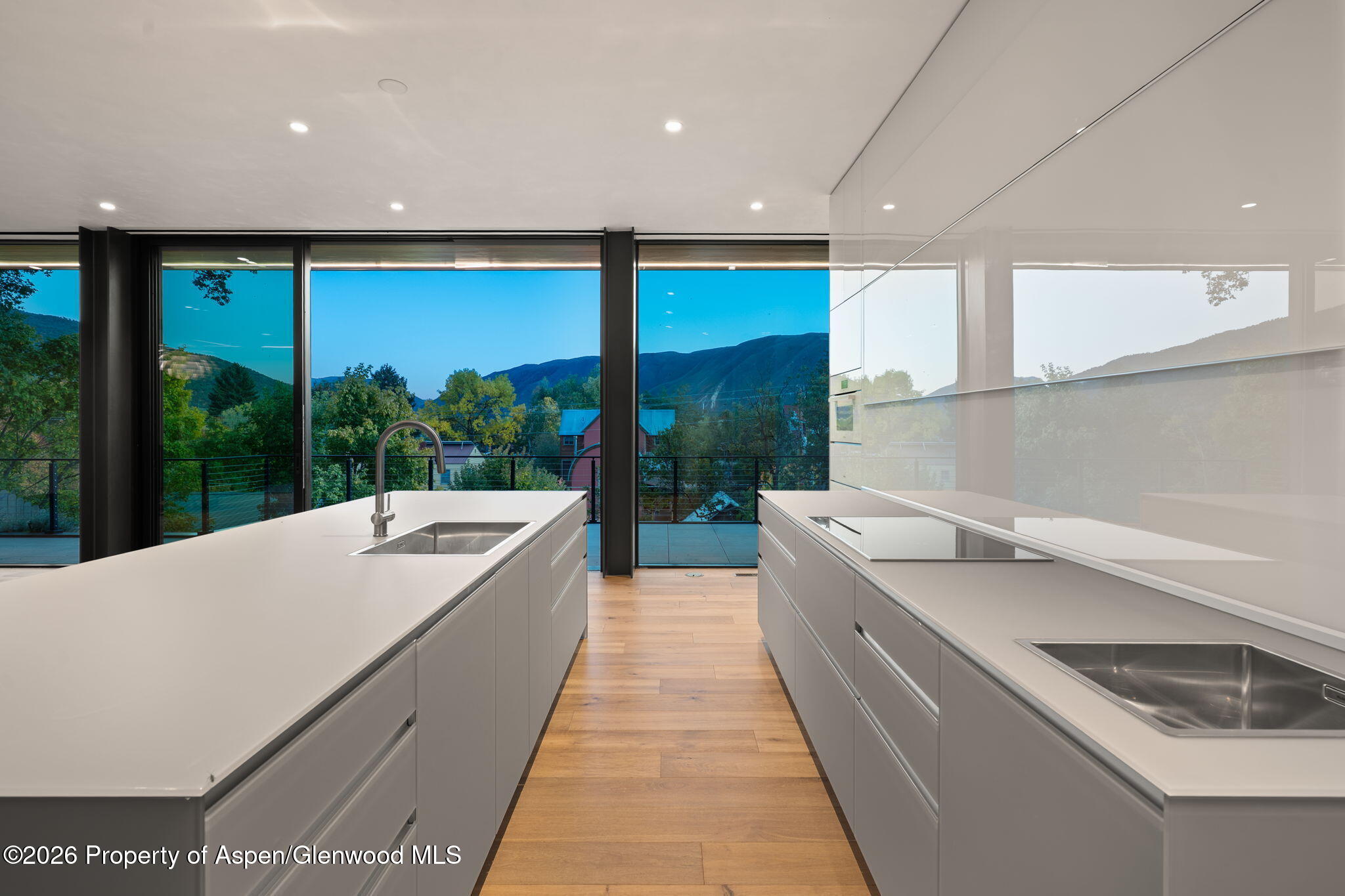 Modern kitchen with twin white islands and expansive windows overlooking a mountain valley.