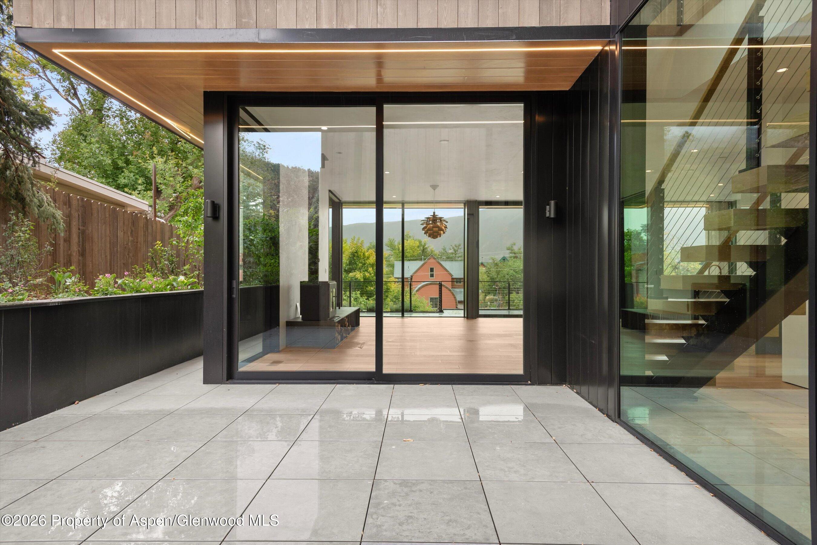 Modern home patio with floor-to-ceiling glass doors, floating staircase, and mountain view.