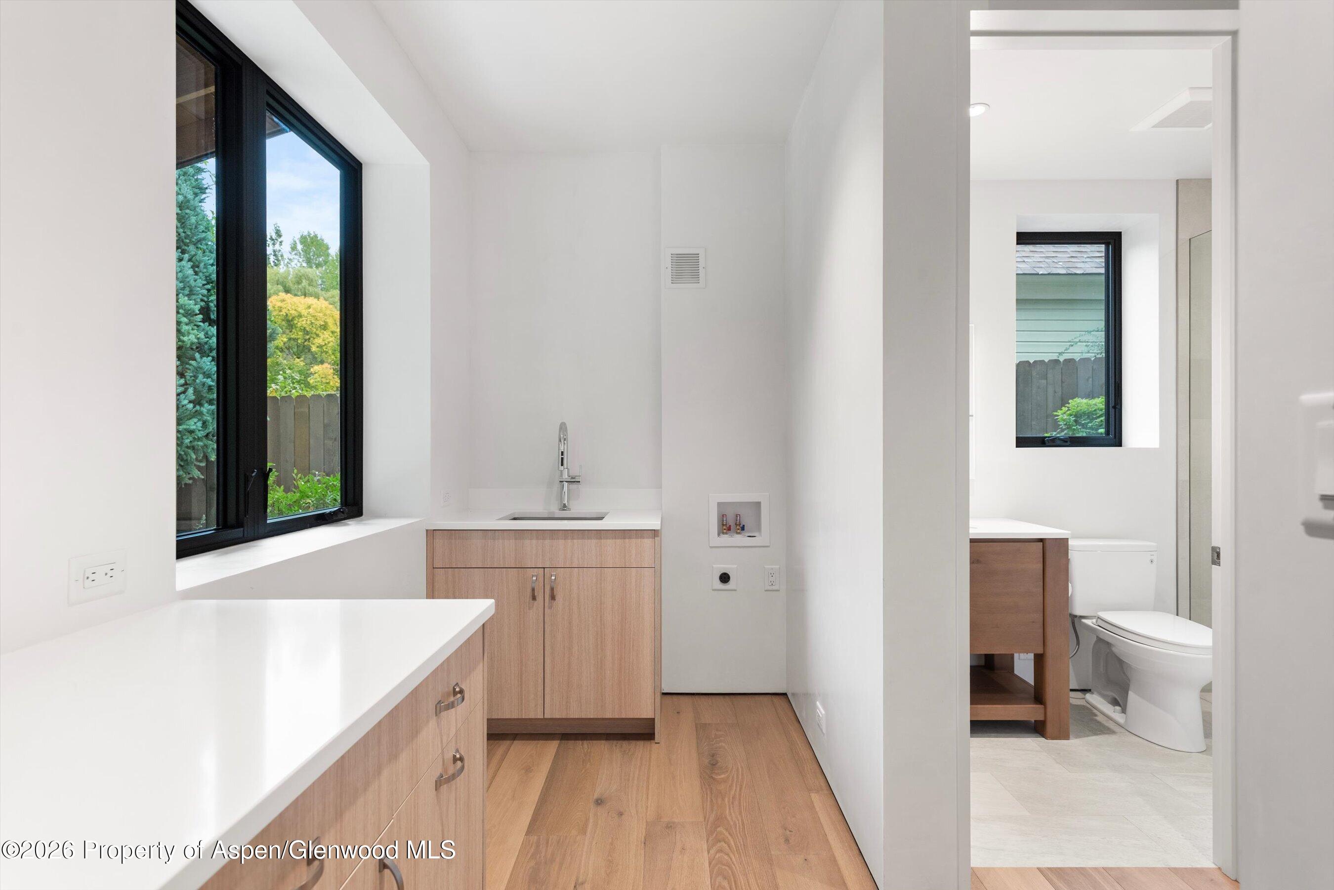 Laundry room with a utility sink and large window beside an adjoining bathroom.