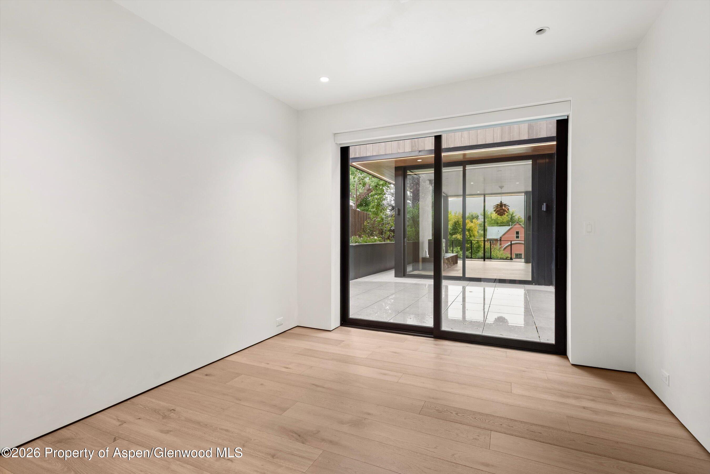 Empty room with light wood floors and sliding glass doors opening onto a covered patio.