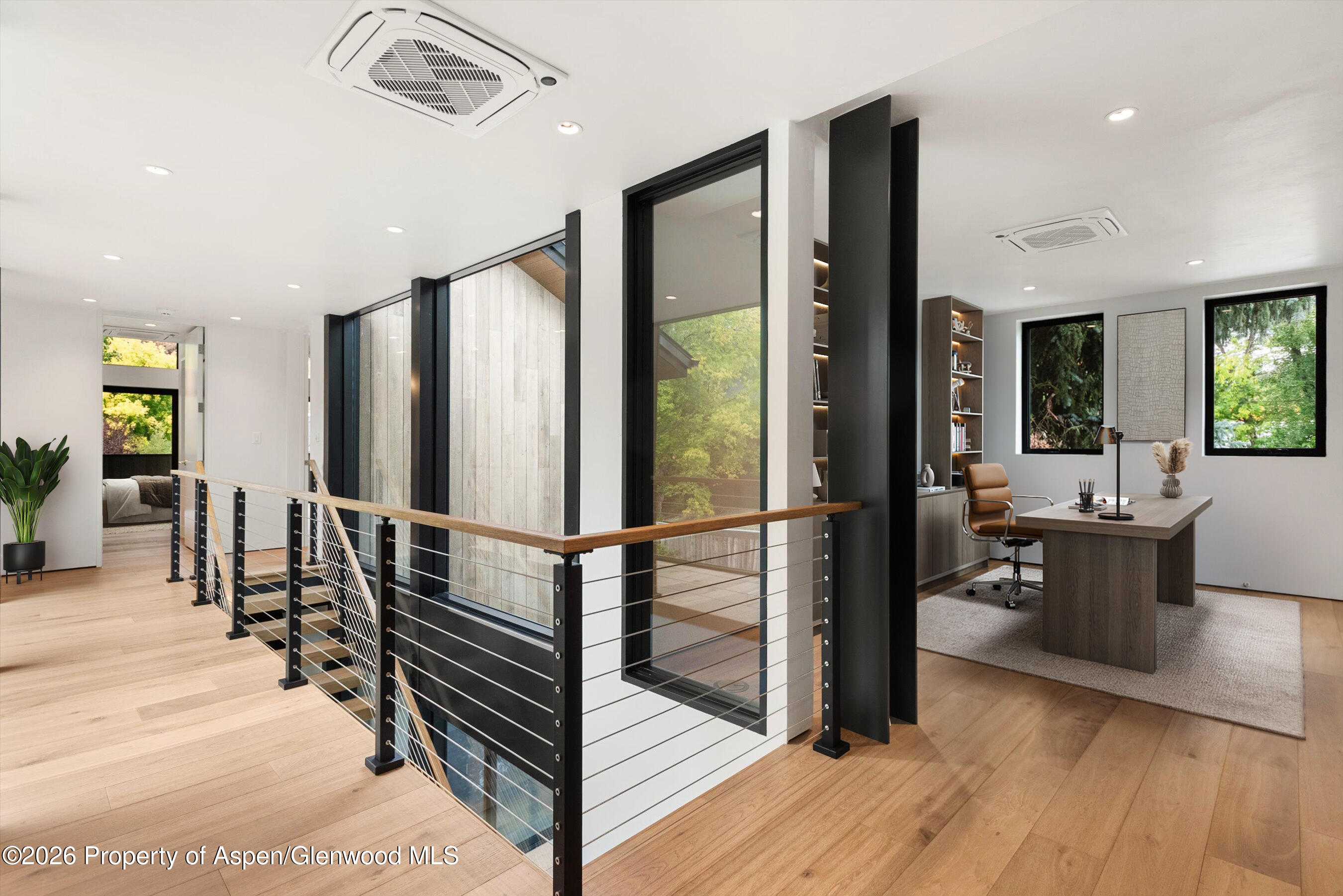Modern landing with cable railing beside a furnished home office with large windows.