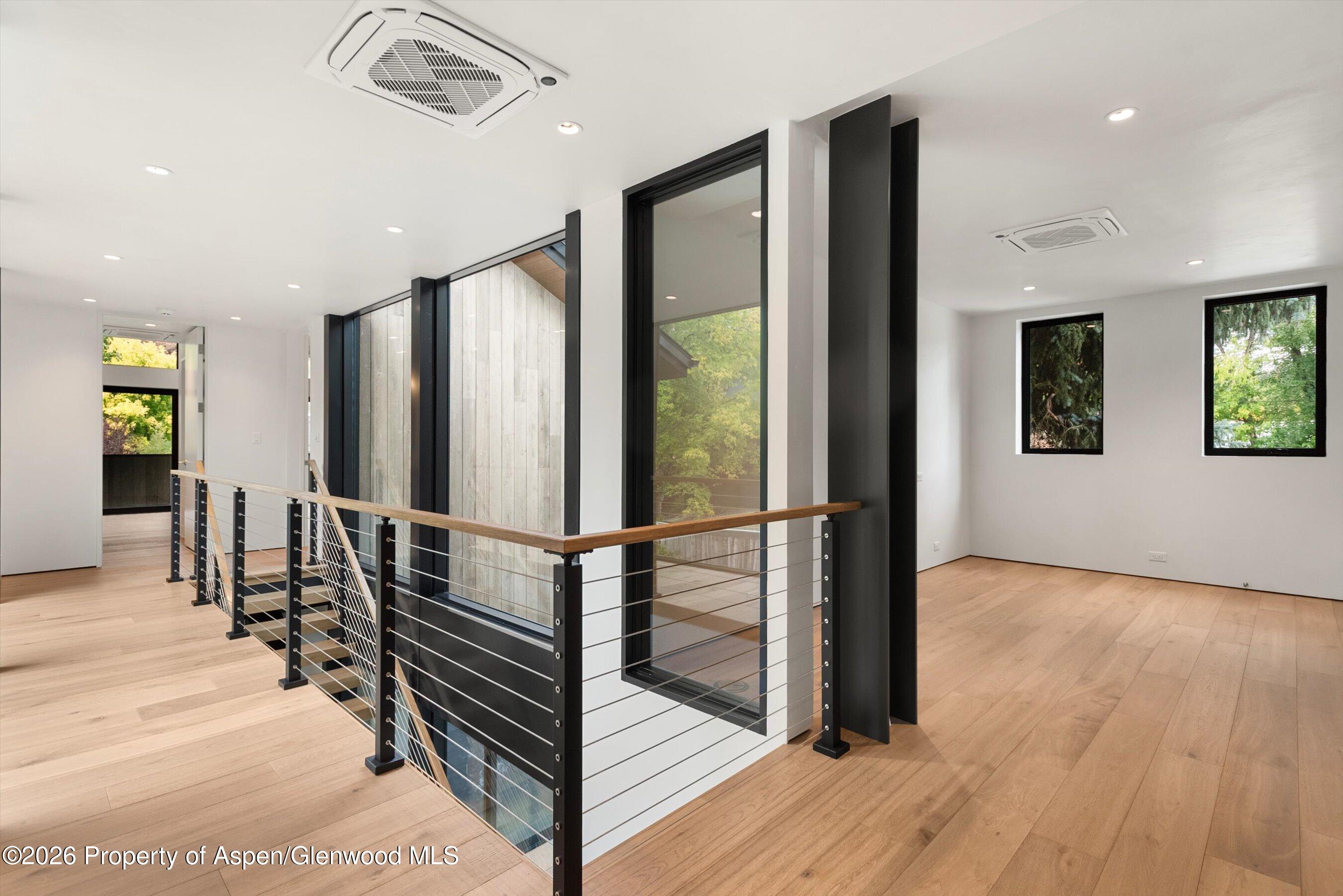 Modern upstairs landing with pale wood floors, black-framed windows, and a cable-railed stairwell.