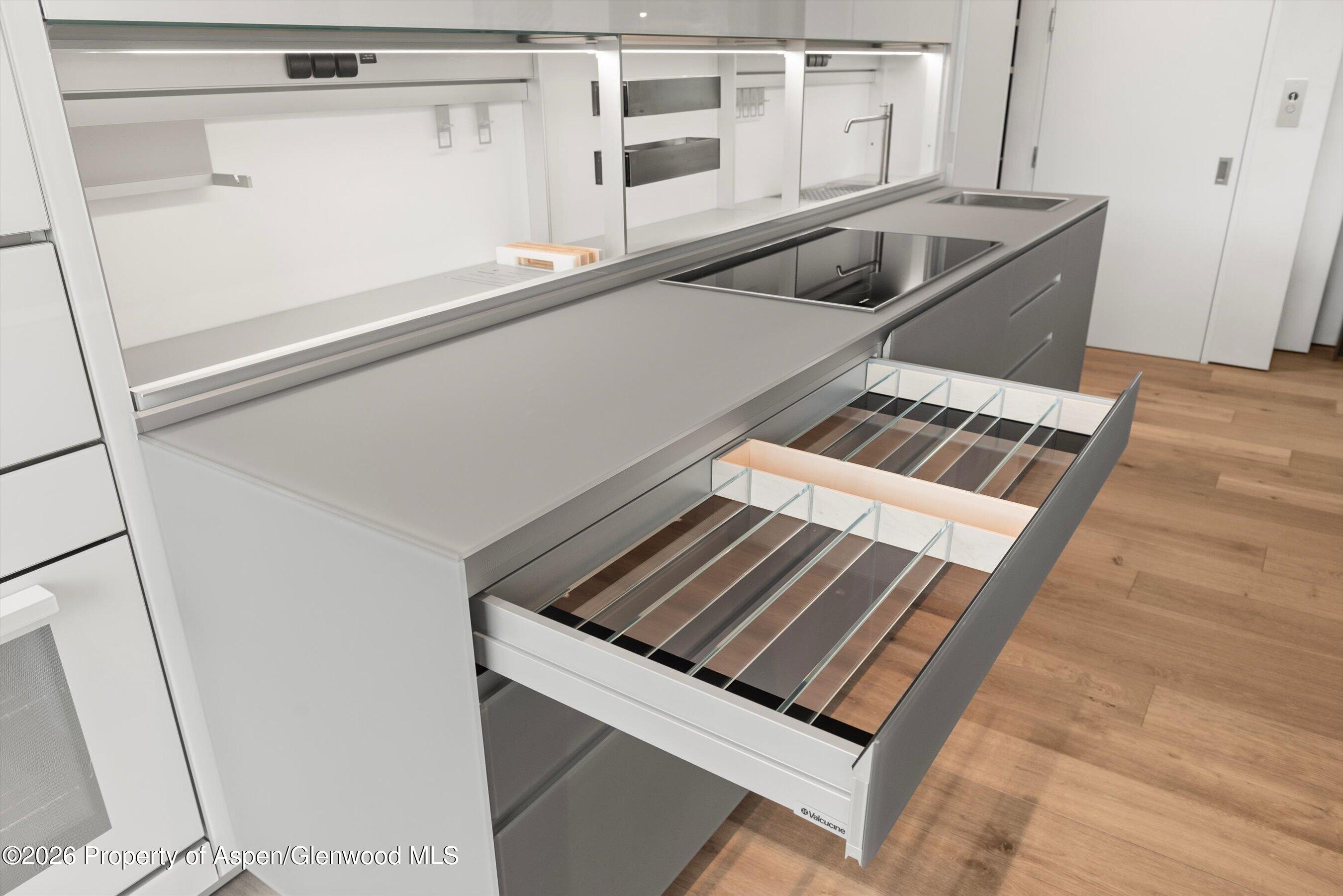 Modern kitchen with deep gray pull-out drawers and glass dividers beside a broad countertop and sink.