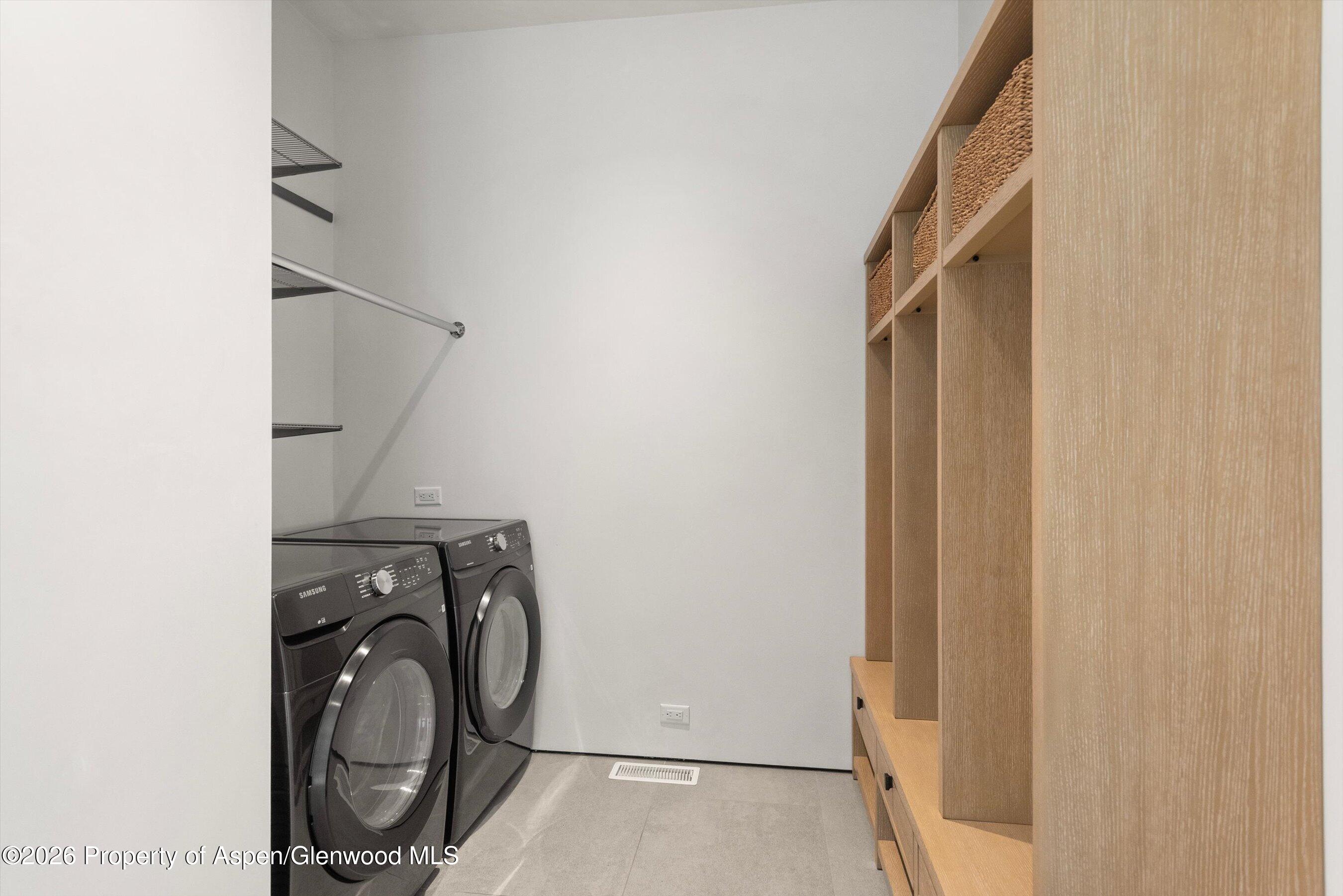 Laundry room with front-loading washer and dryer beside built-in wood shelves and woven baskets.