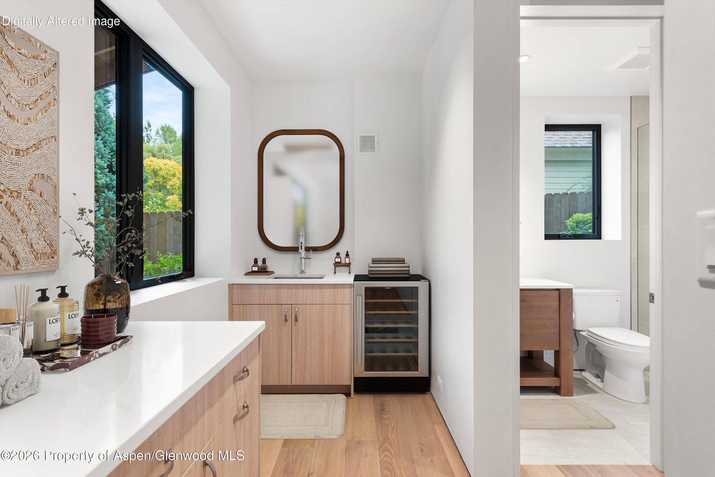 Bathroom with a light wood vanity, rounded mirror, beverage refrigerator, and separate toilet room.