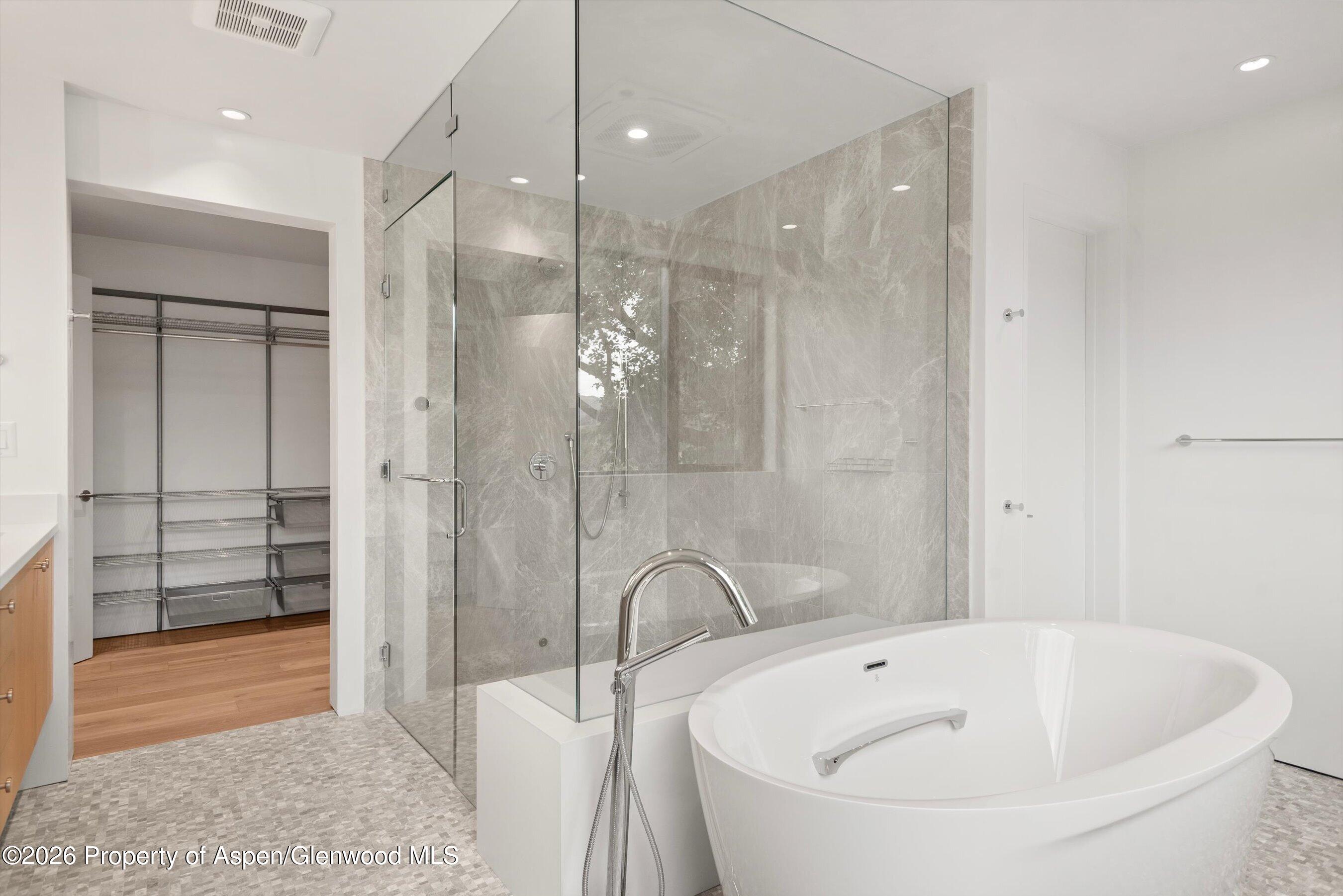 Modern bathroom with a freestanding soaking tub, glass shower, and open walk-in closet.