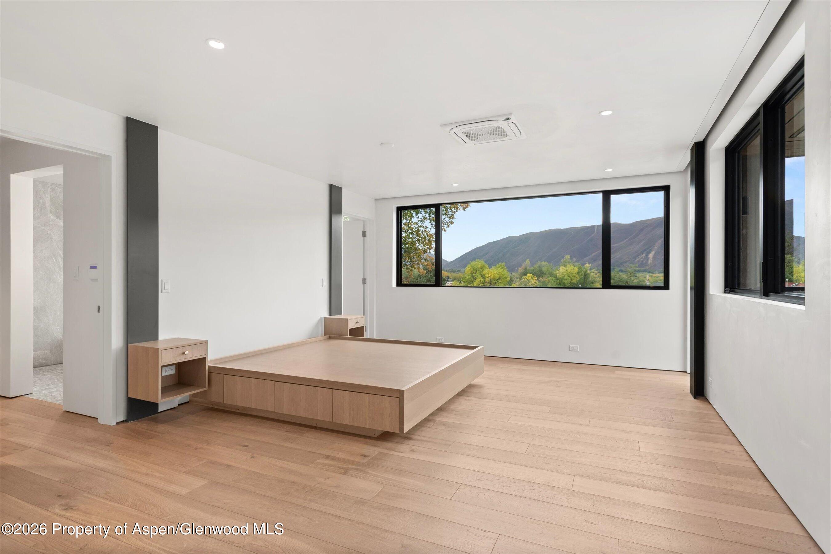 Modern bedroom with a built-in wood platform bed and mountain views through wide windows.