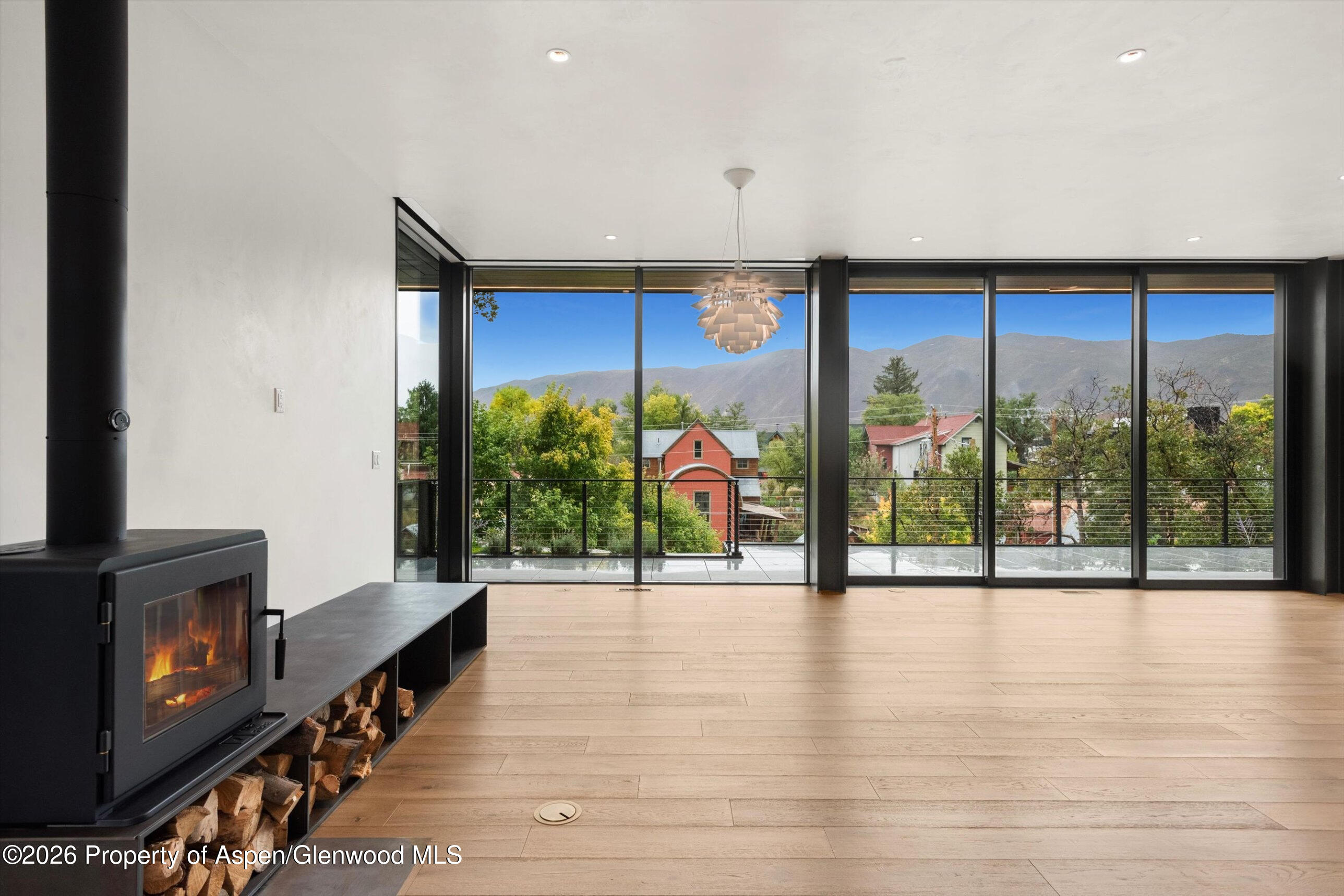 Vacant living room with a wood-burning fireplace and wide windows overlooking autumn trees and mountains.