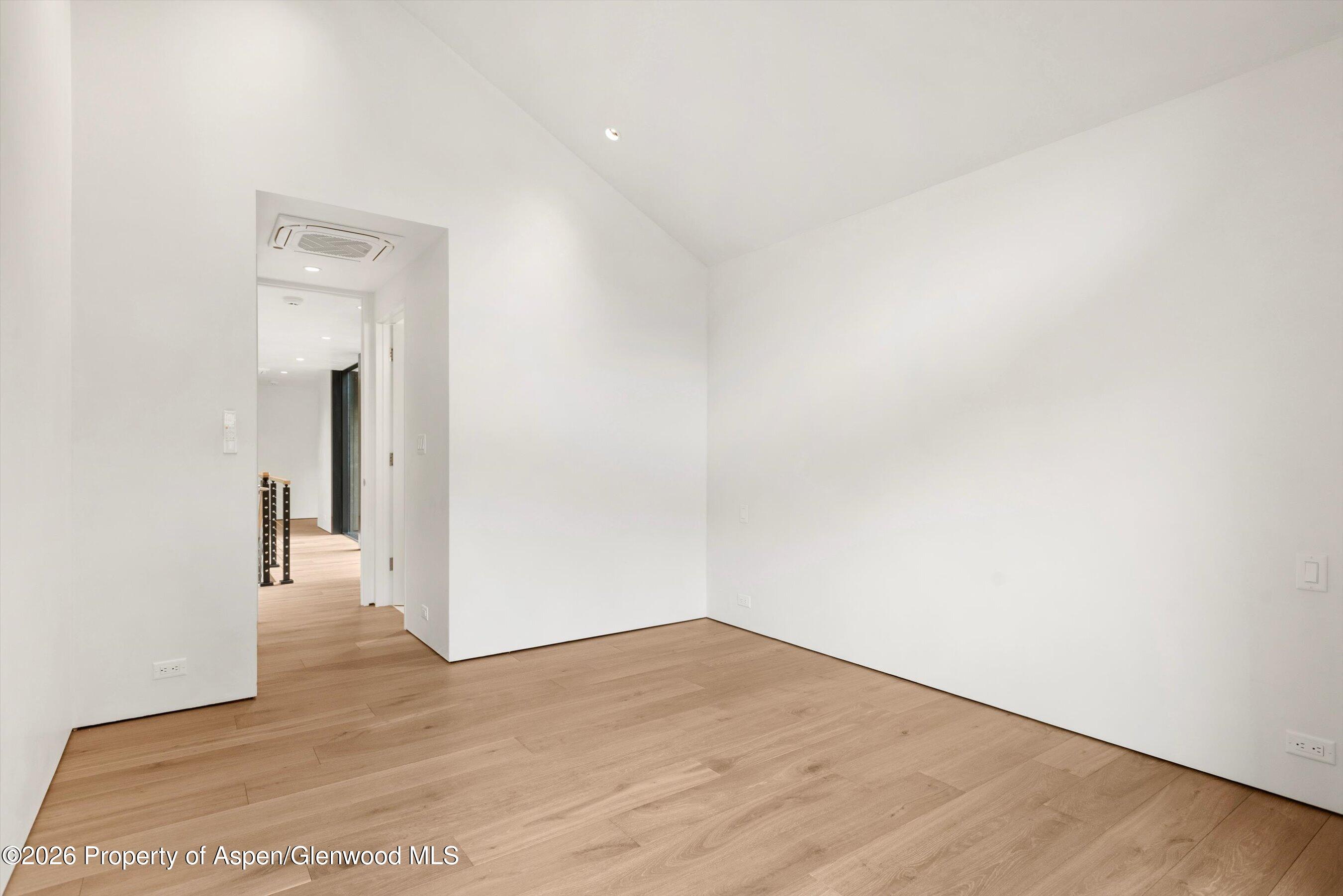 Vacant room with light wood floors, white walls, and an open doorway to the hallway.