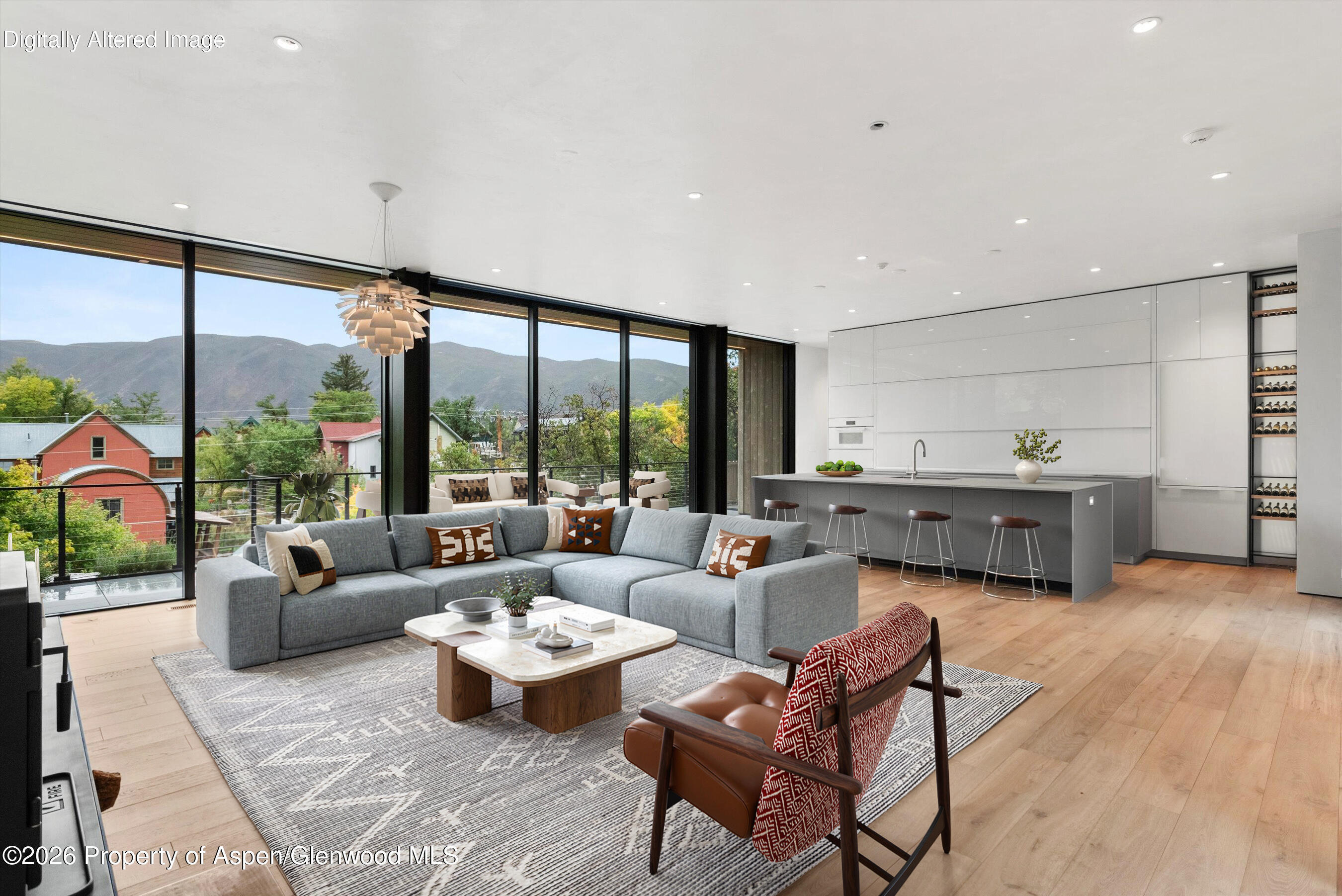 Open-plan living room and kitchen with a gray sectional, long island, and mountain views through floor-to-ceiling windows.